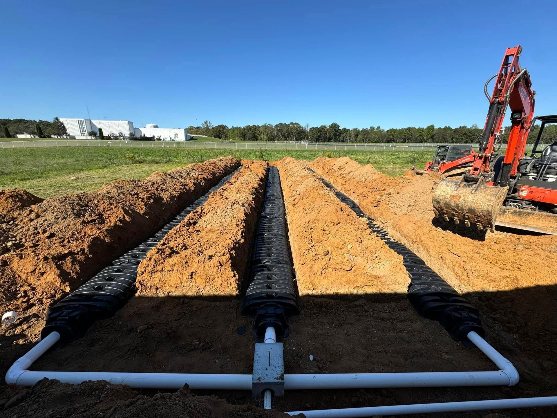 A man is digging a trench in the dirt with a tractor in the background.