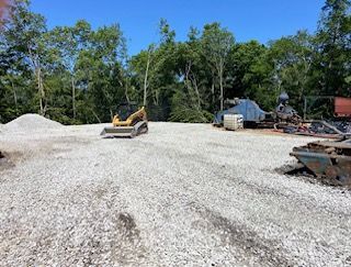 Construction site with white gravel piles, a skid steer, and heavy equipment under blue sky