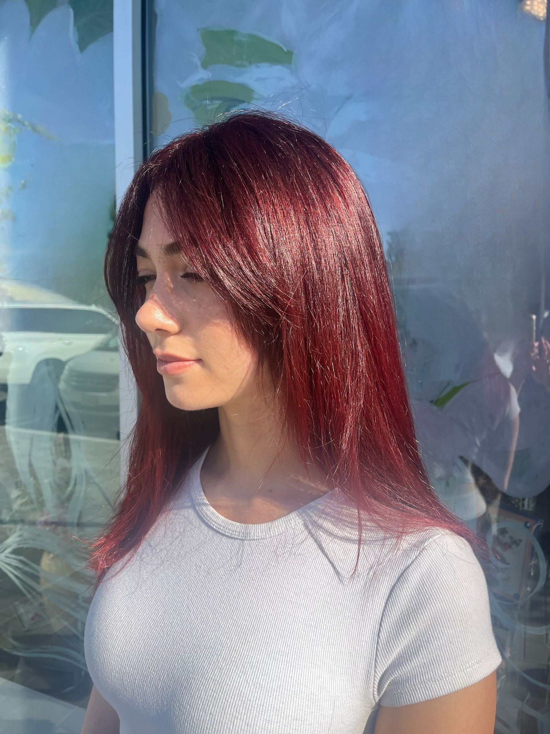 A woman with red hair and a white shirt is standing in front of a window.