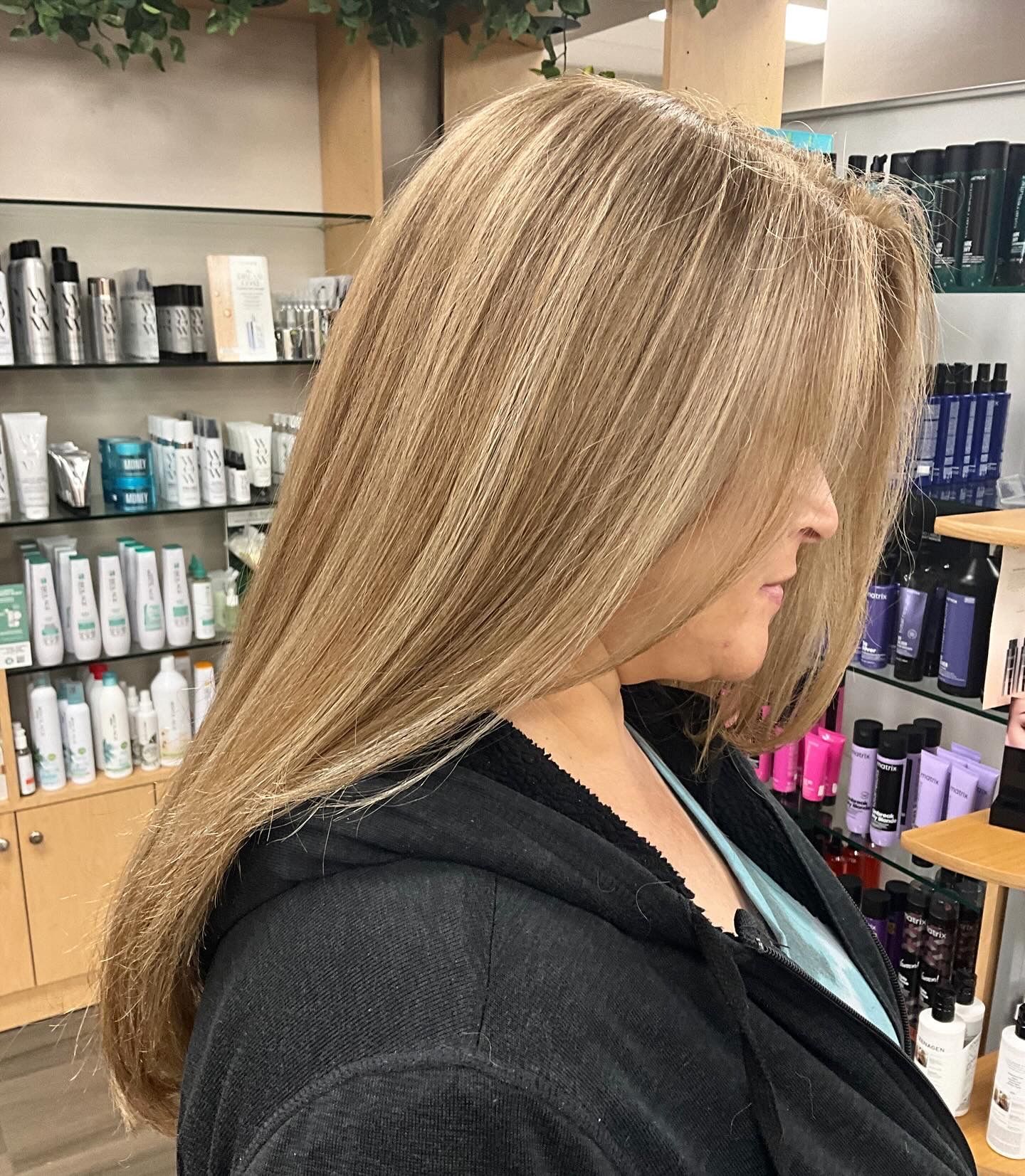 A woman with long blonde hair is standing in front of a display of hair products.