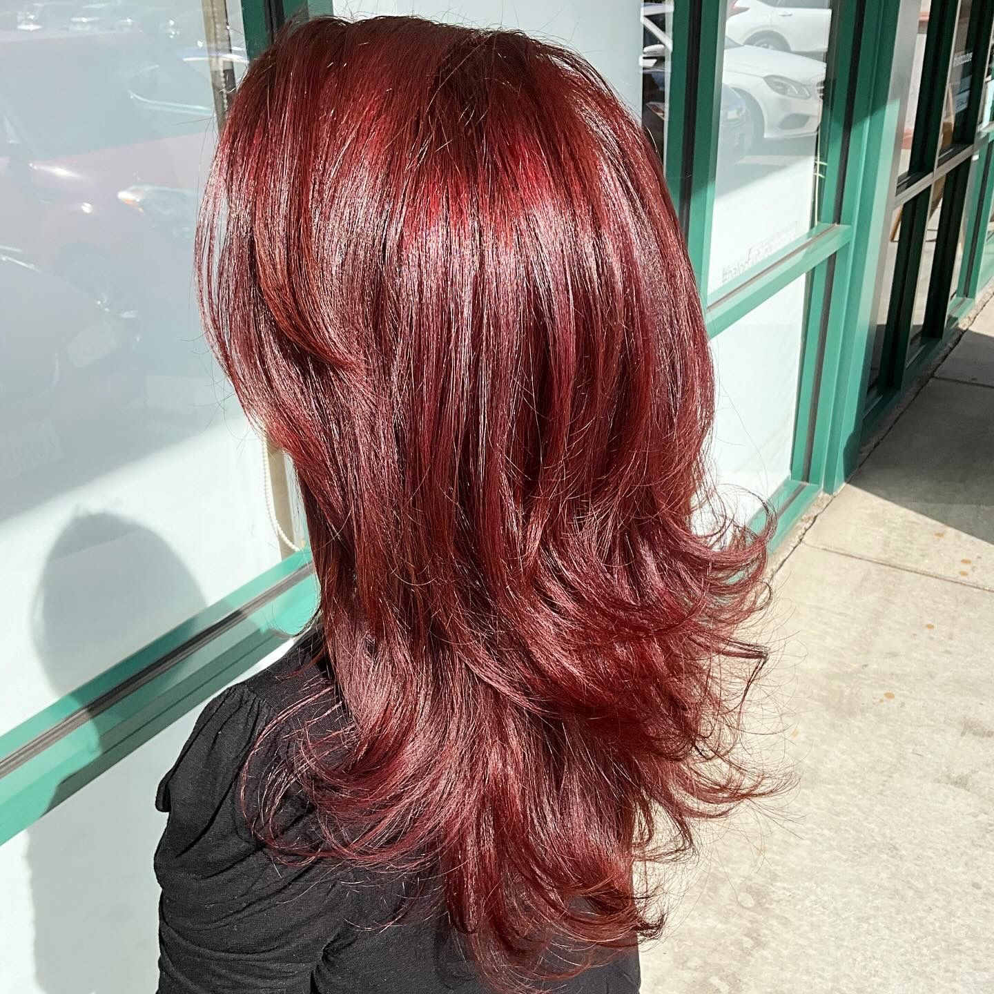 A woman with long red hair is standing in front of a window