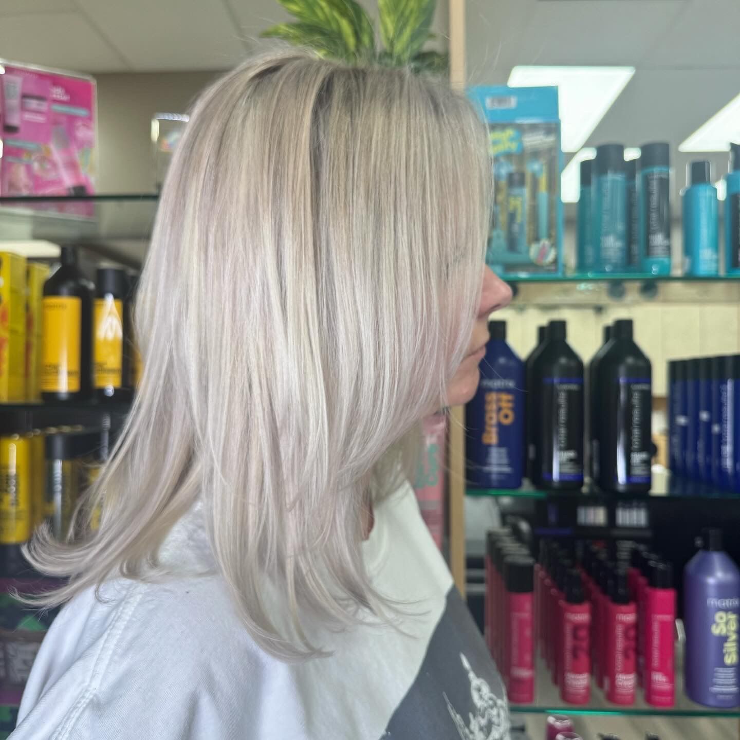 A woman with blonde hair is standing in front of a shelf of hair products.