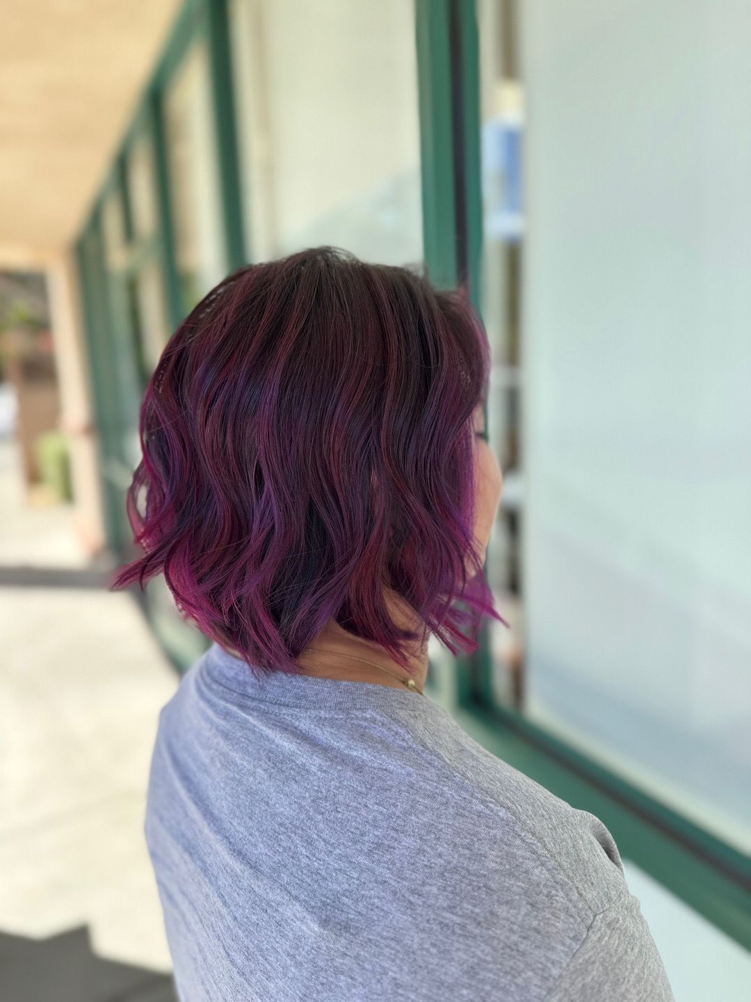 A woman with purple hair is standing in front of a window.