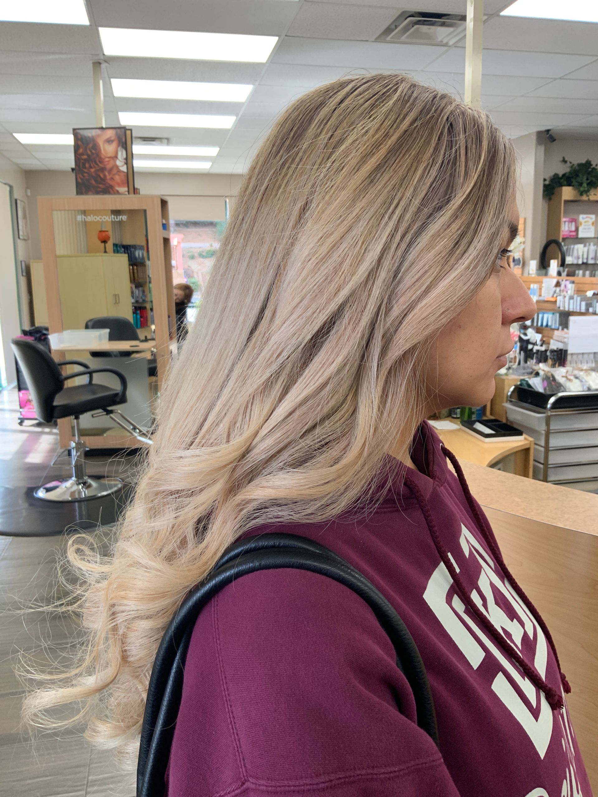 A woman in a purple sweatshirt is standing in a hair salon.