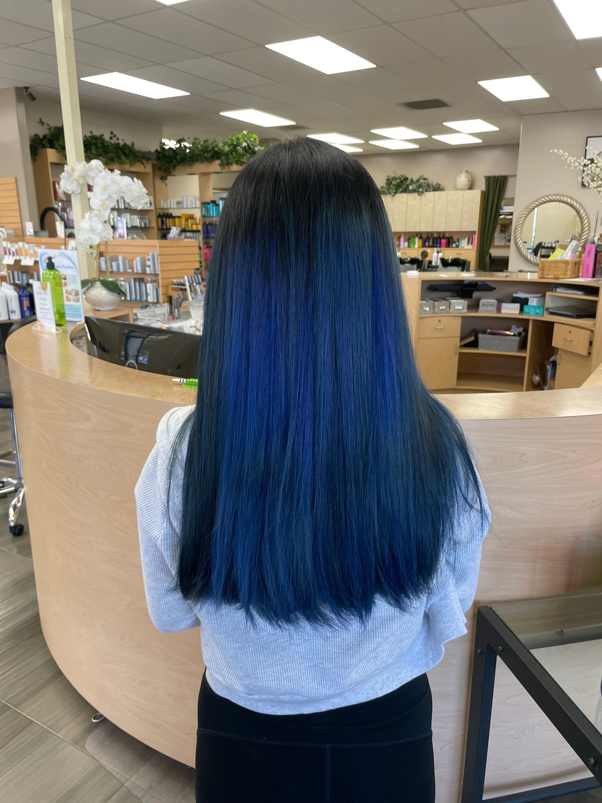 A woman with blue hair is standing in front of a counter in a salon.