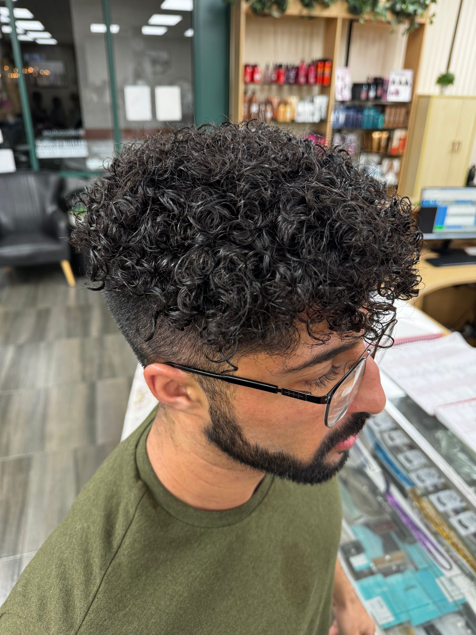 A man with curly hair and glasses is standing in a barber shop.