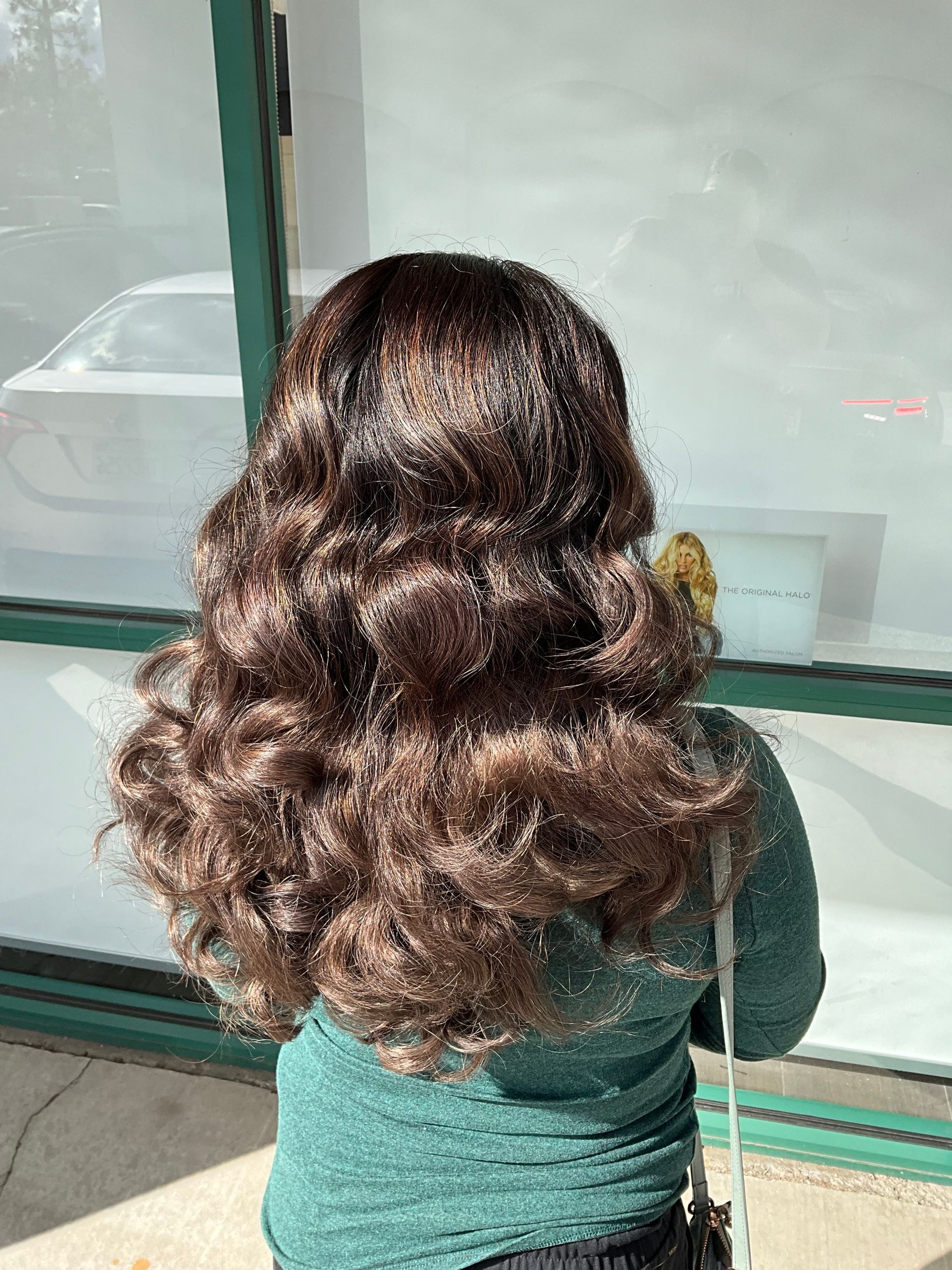 A woman with long curly hair is standing in front of a window.