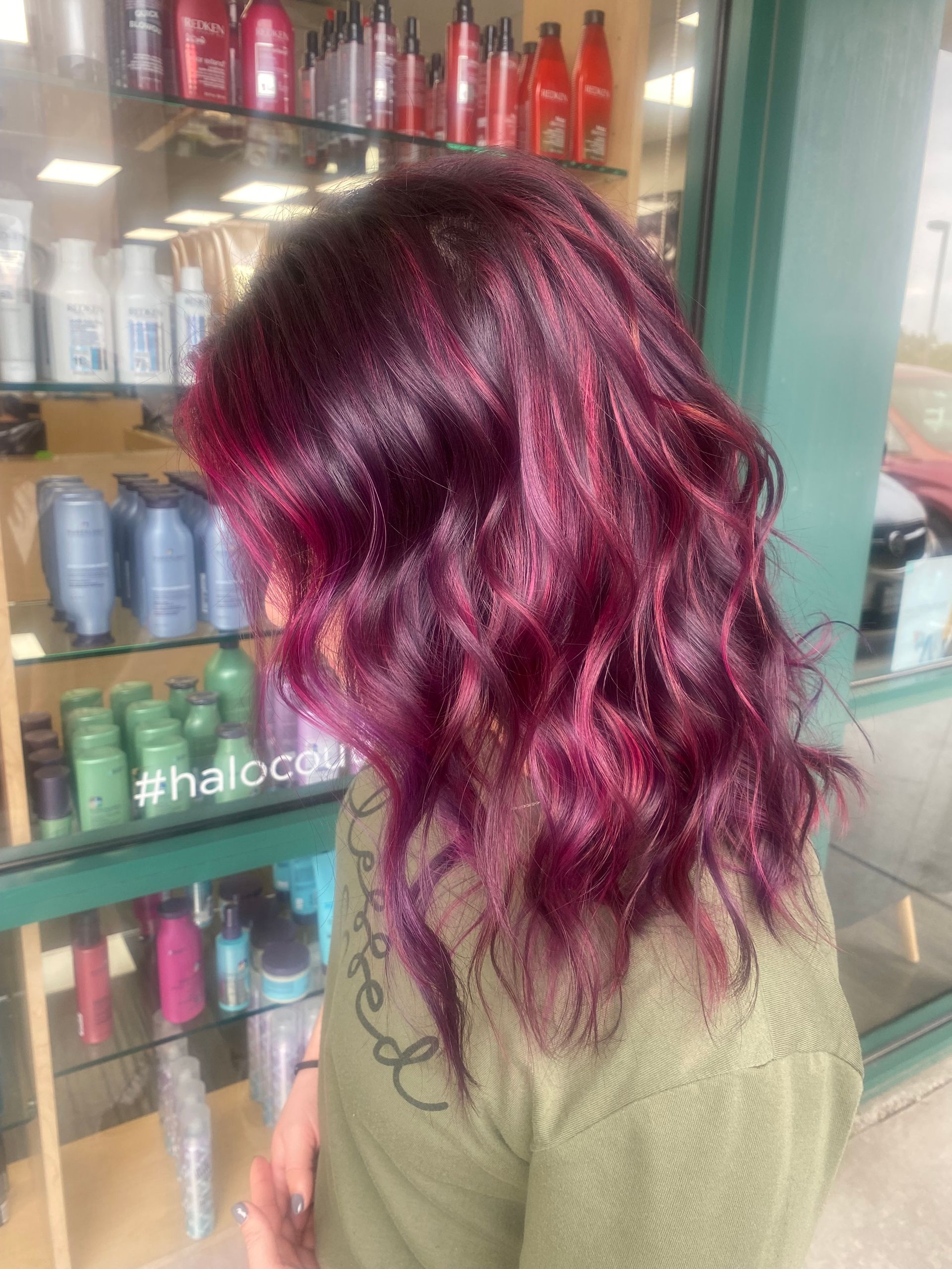 A woman with purple hair is standing in front of a store.