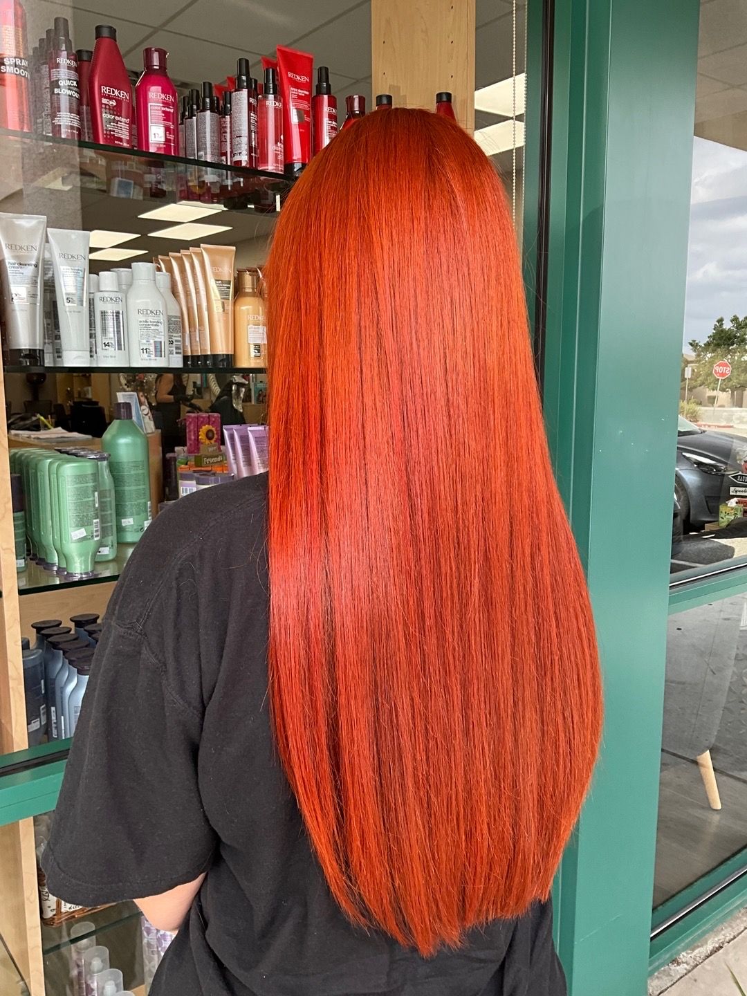 A woman with long red hair is standing in front of a store window.