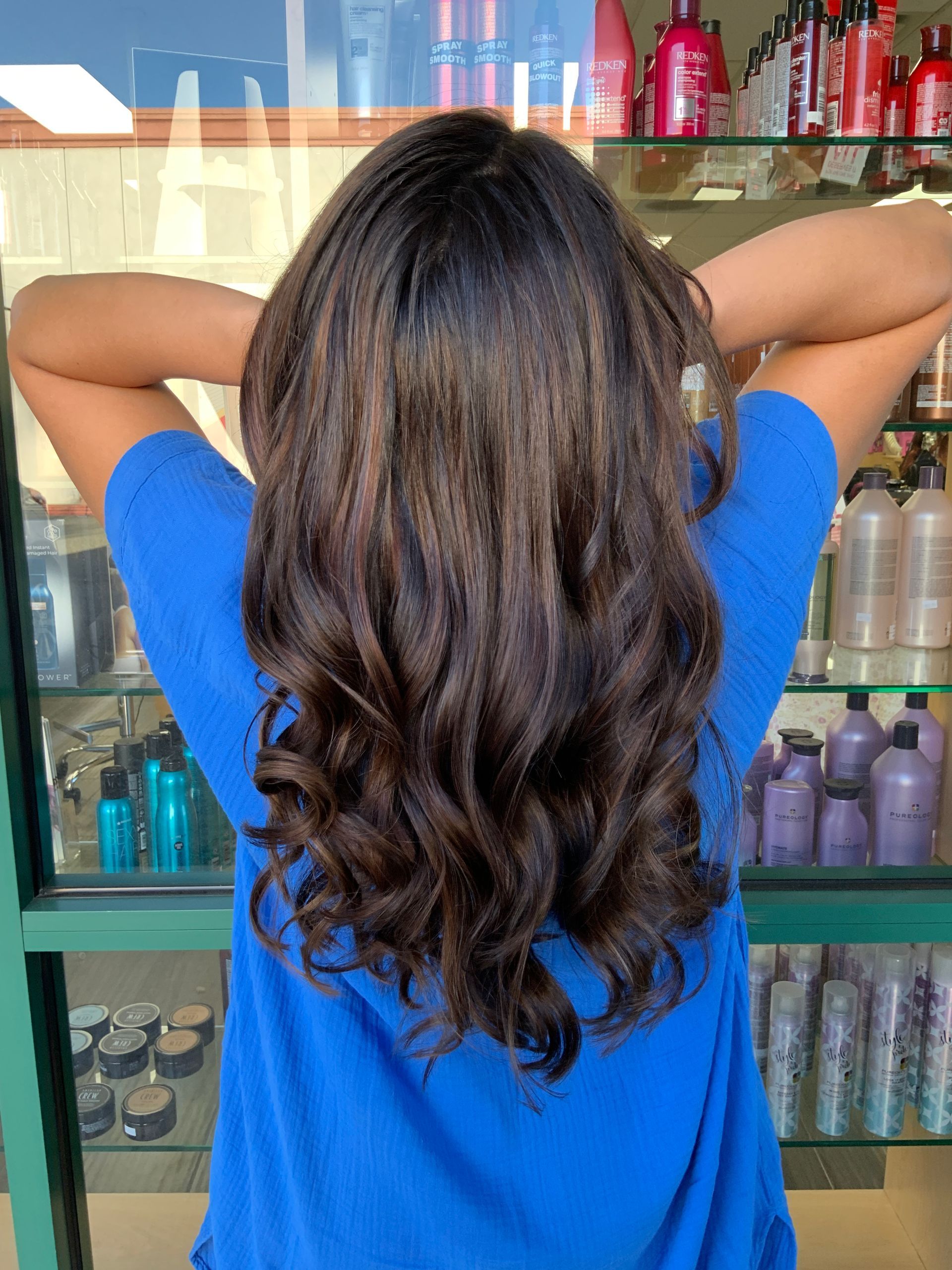 A woman in a blue shirt is standing in front of a display of hair products.