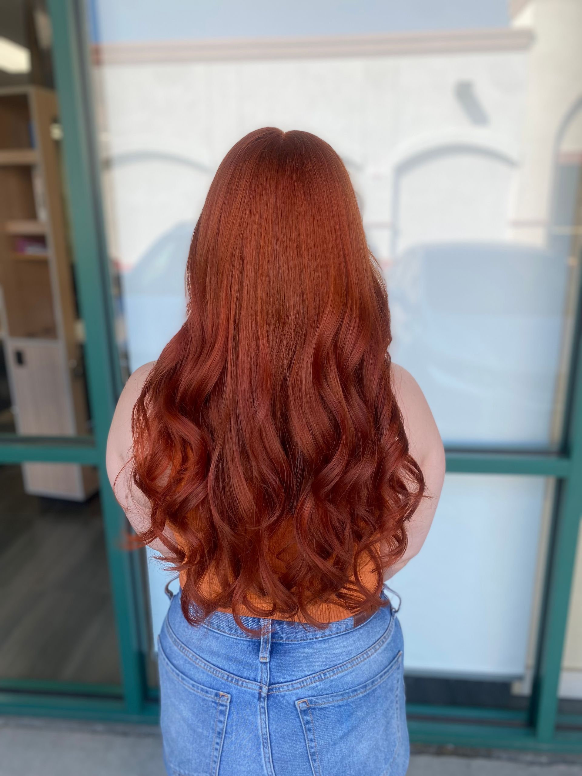 A woman with long red hair is standing in front of a window.