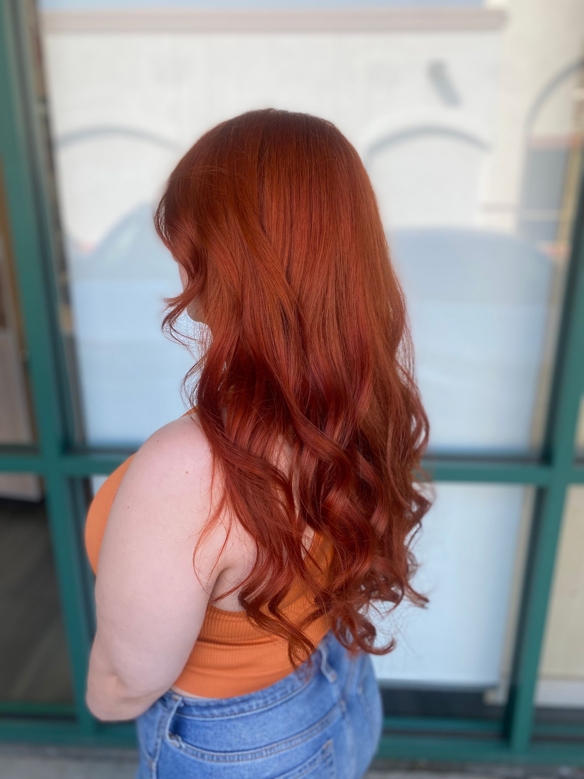 A woman with long red hair is standing in front of a window.