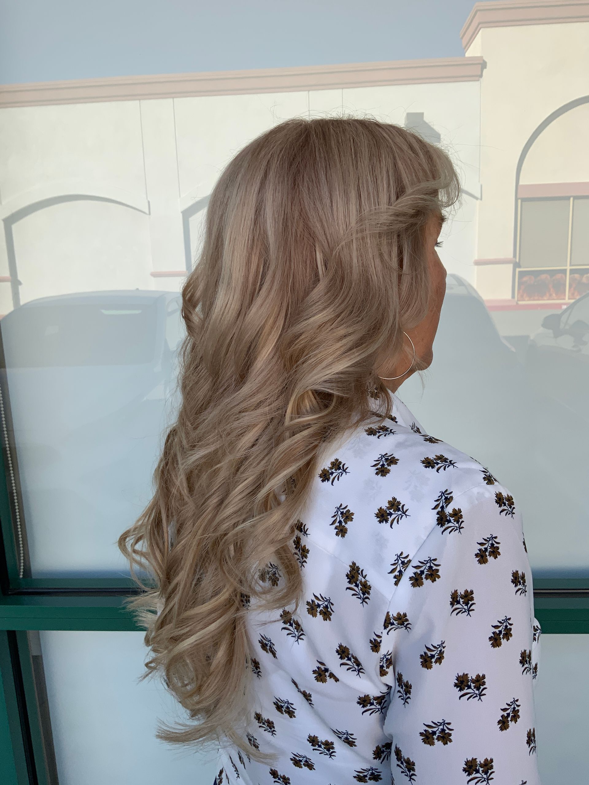 A woman with long blonde hair is standing in front of a window.