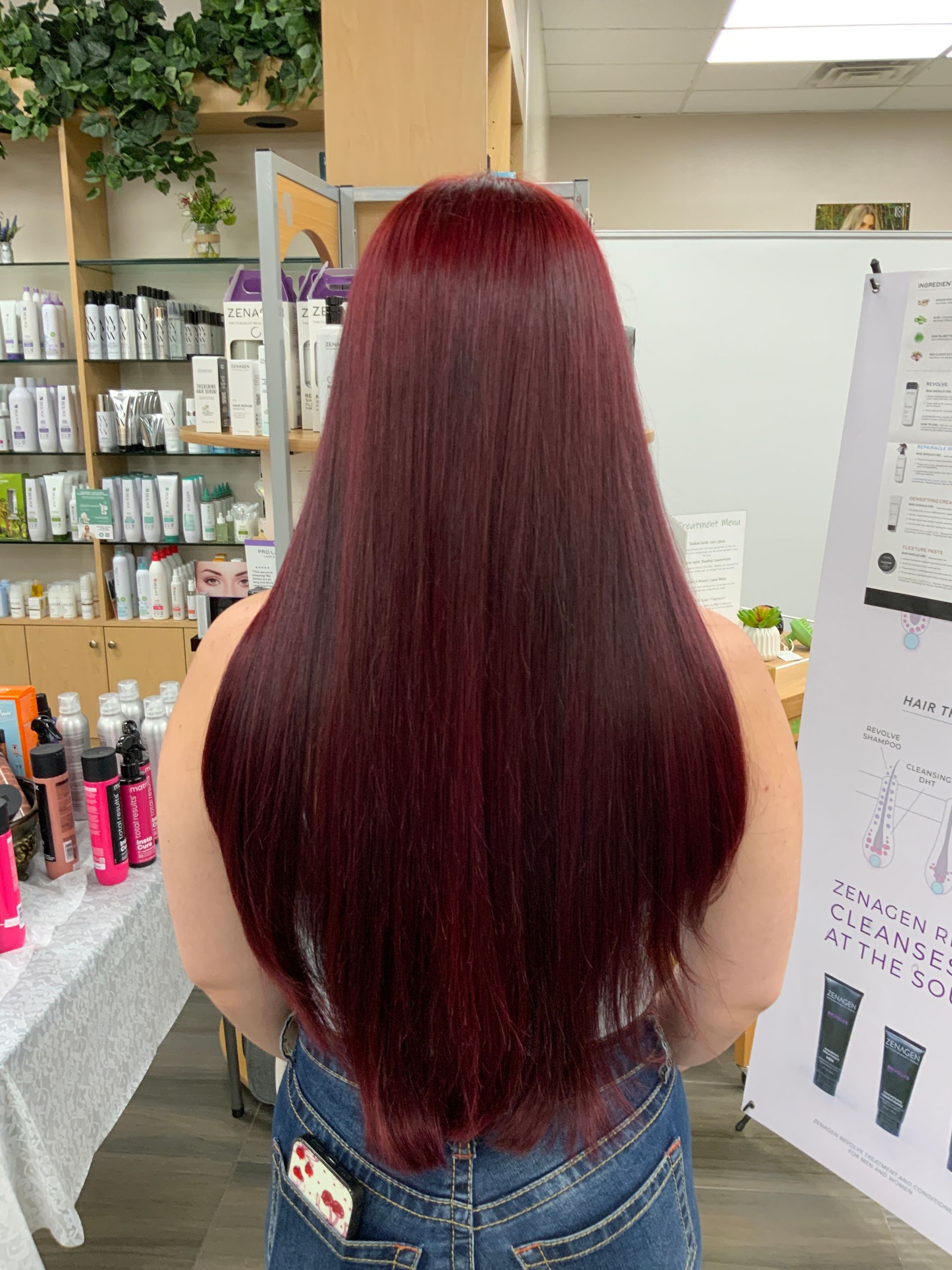 A woman with long red hair is standing in front of a display of hair products.