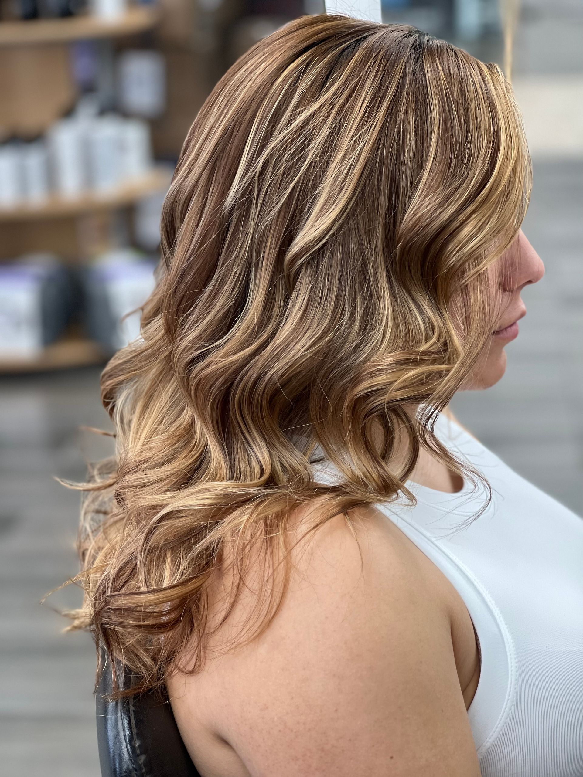 A woman with long brown hair is sitting in a chair in a salon.