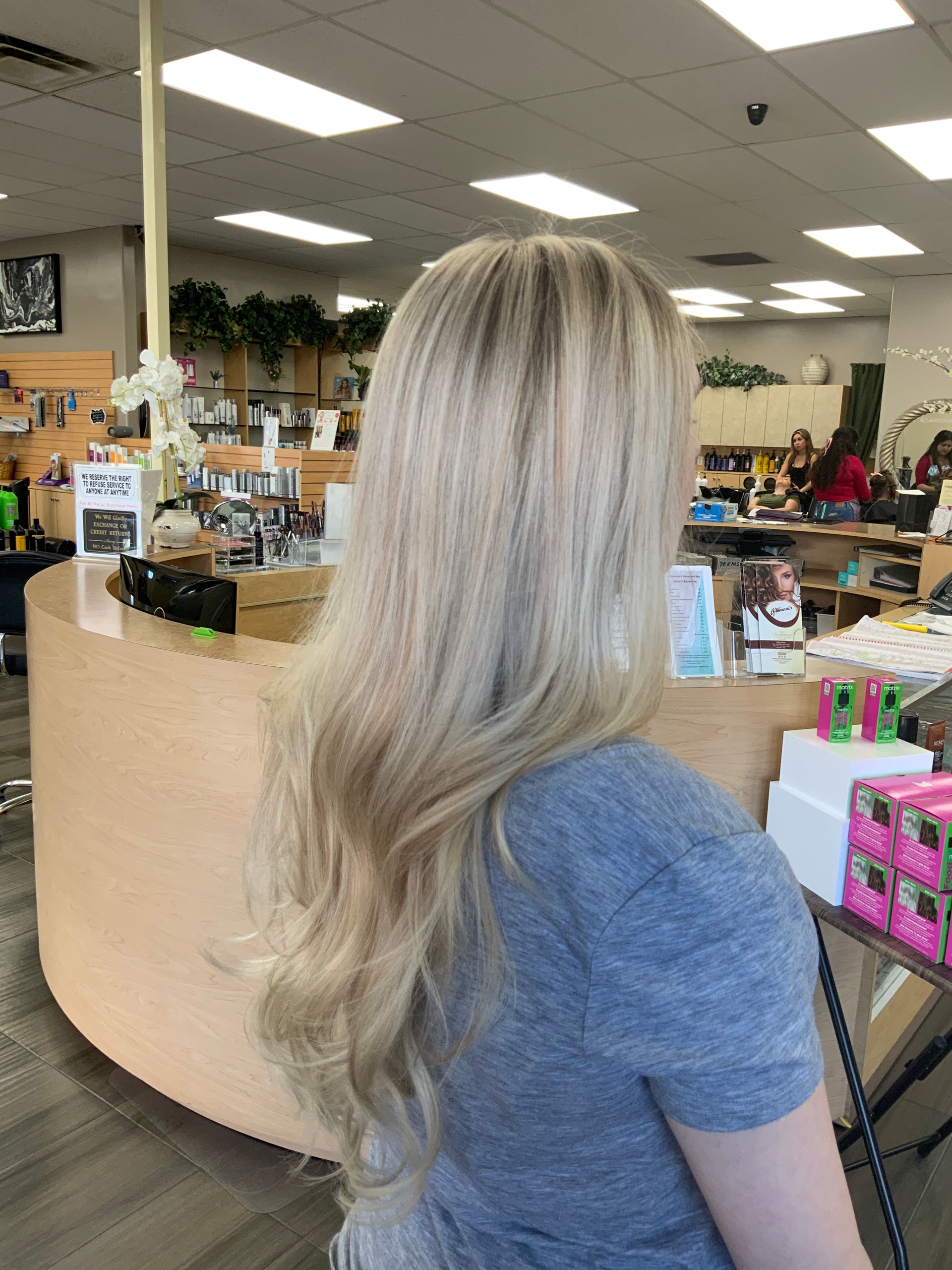 A woman with long blonde hair is sitting at a counter in a salon.
