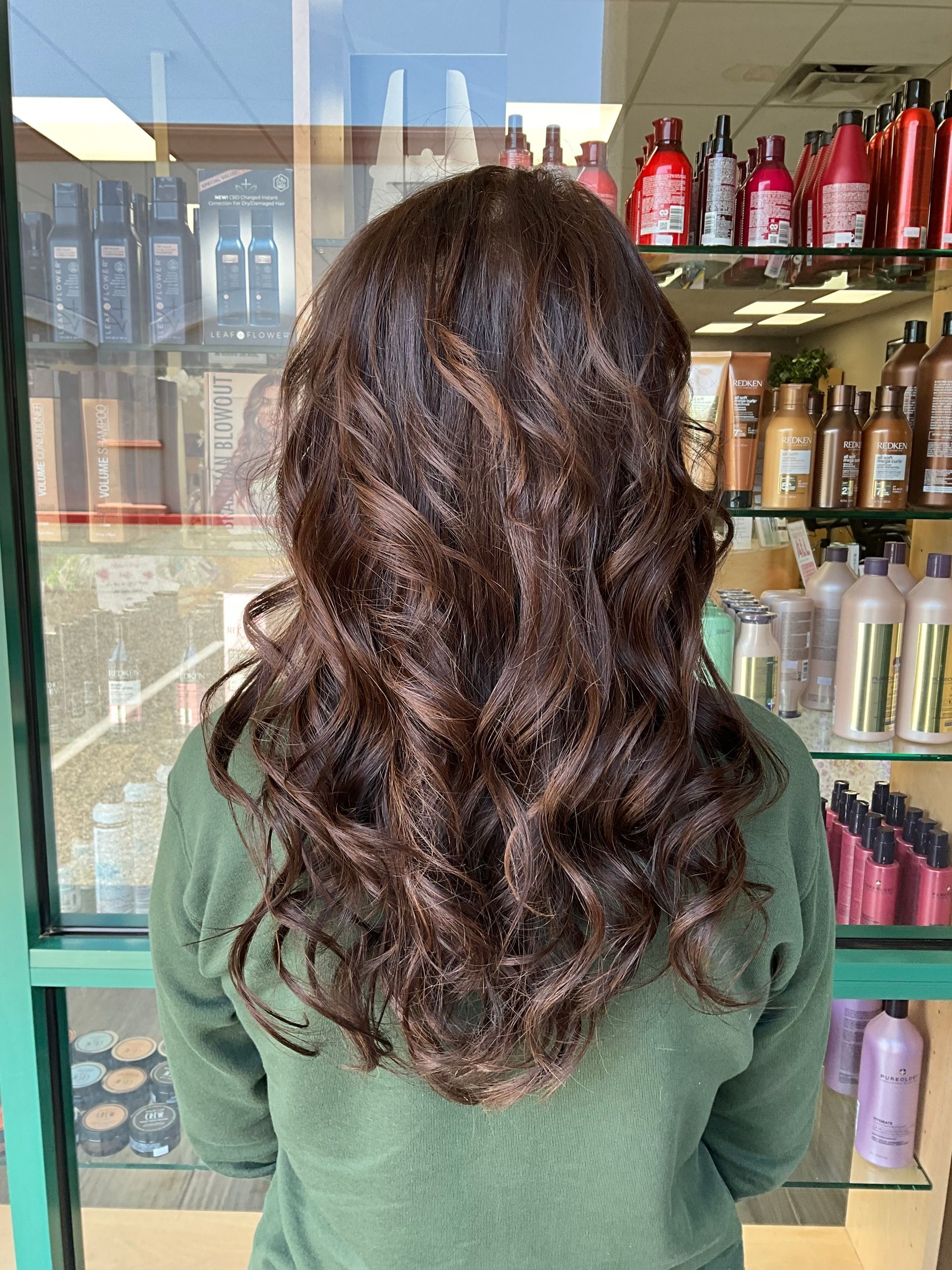 A woman with long brown hair is standing in front of a display of hair products.