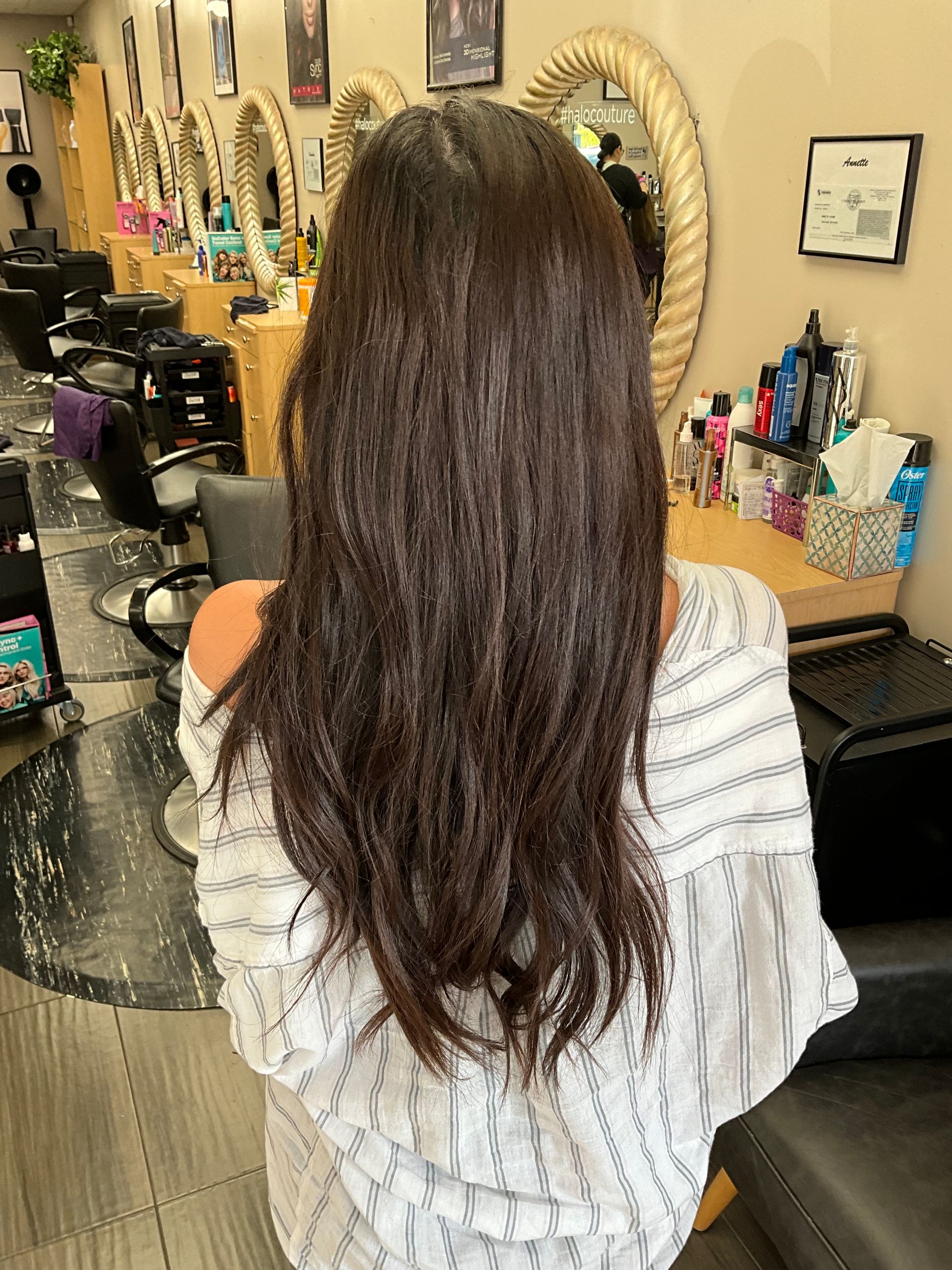A woman is sitting in a hair salon with her back to the camera.