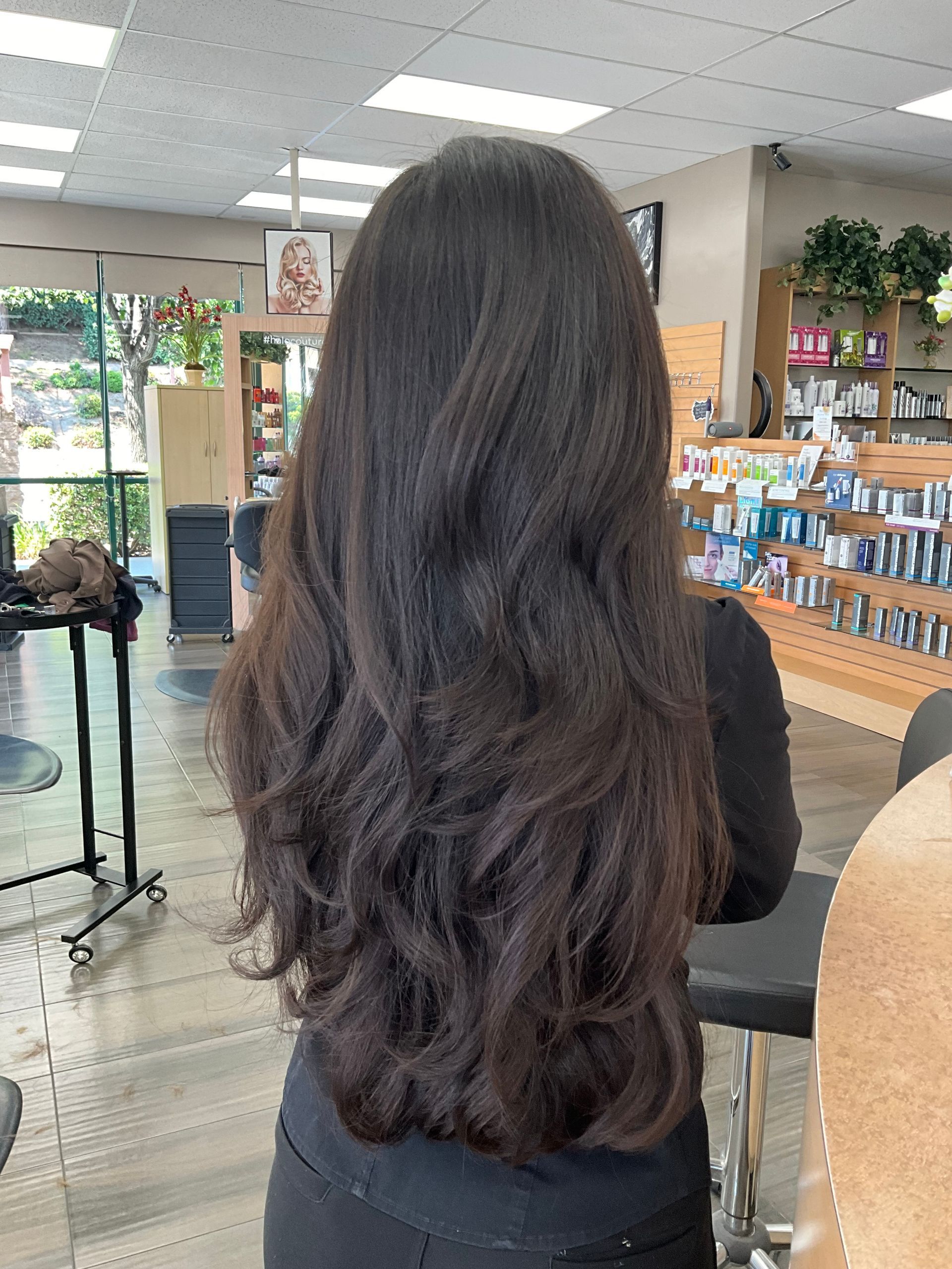A woman with long dark hair is standing in a salon.