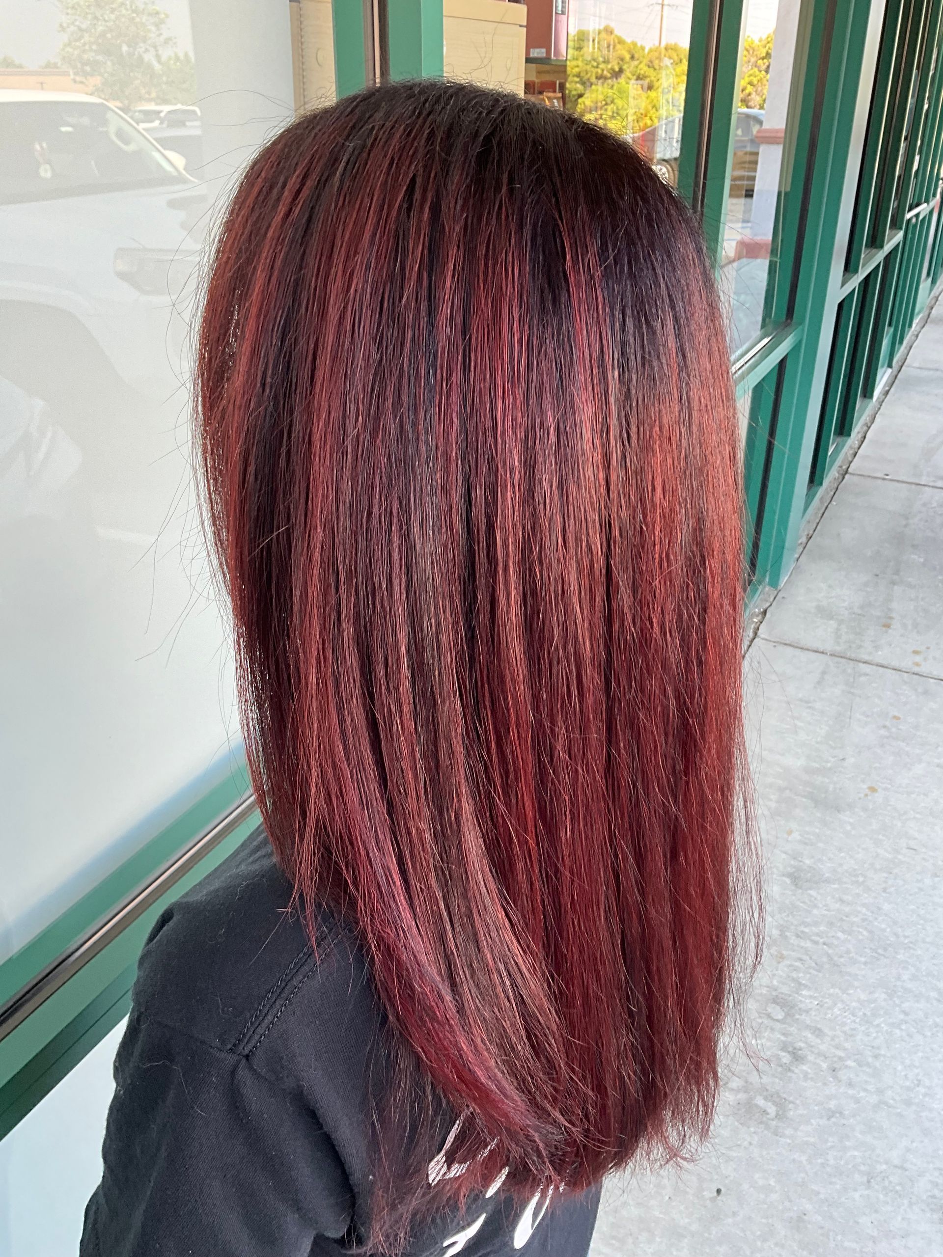 A woman with red hair is standing on a sidewalk in front of a building.