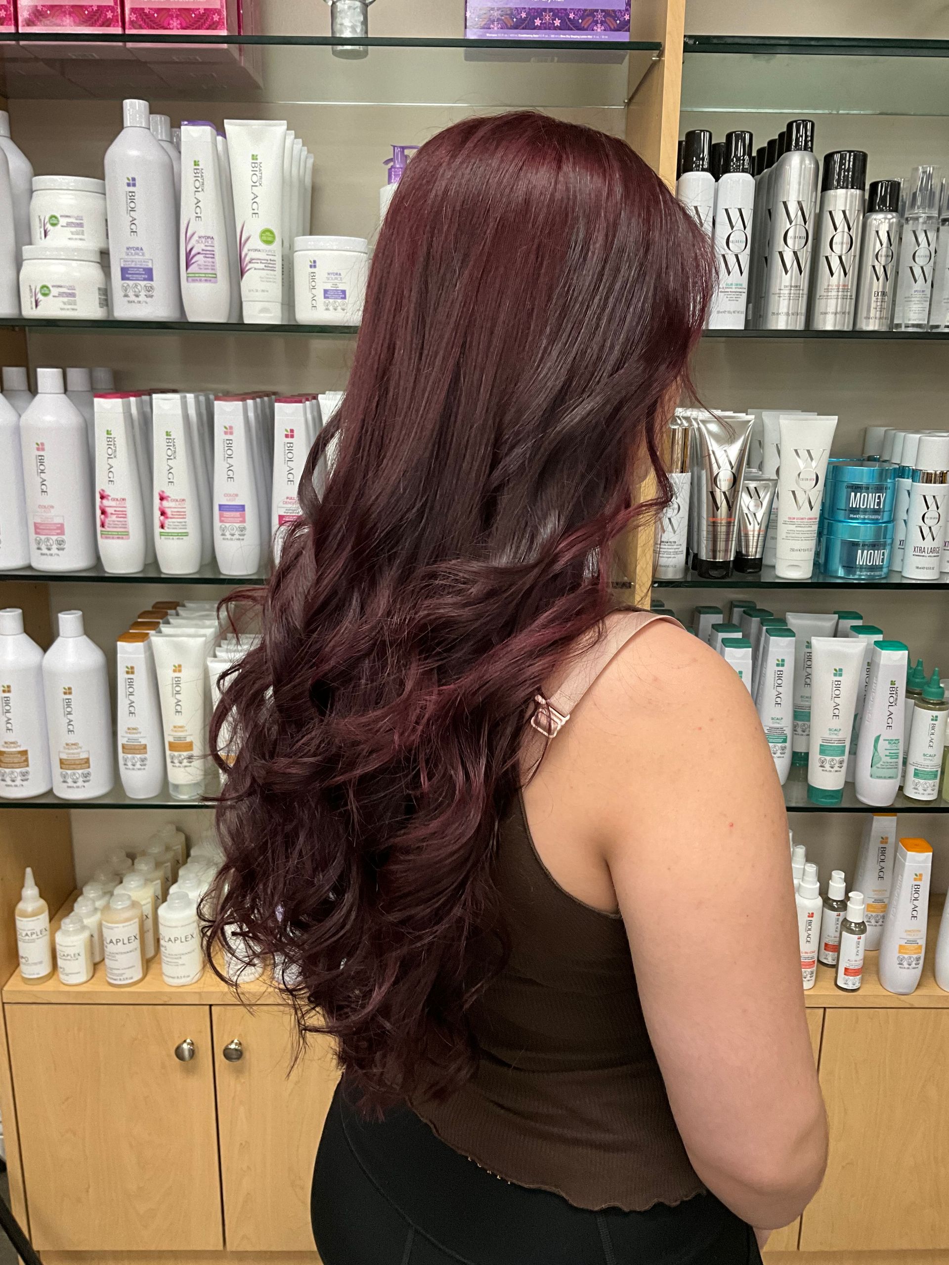 A woman with long red hair is standing in front of a shelf full of hair products.