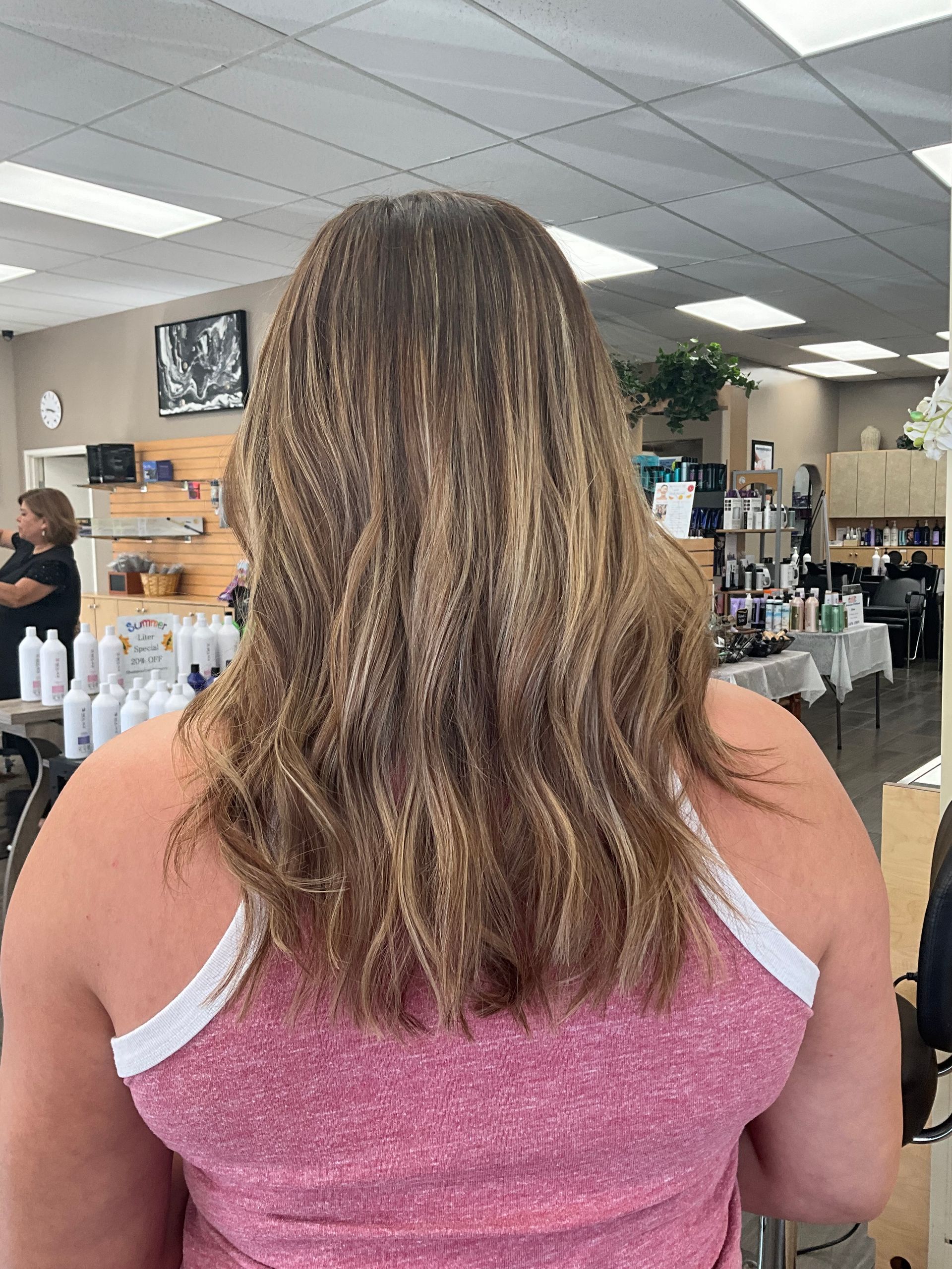 A woman in a pink tank top is standing in a salon with her back to the camera.