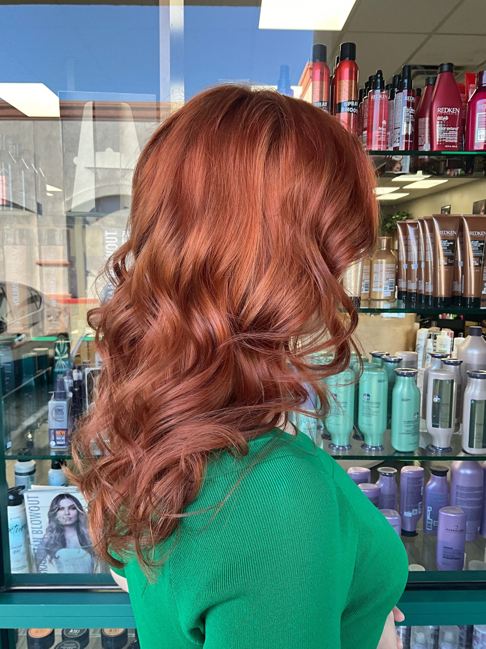 A woman with red hair is wearing a green sweater in a hair salon.