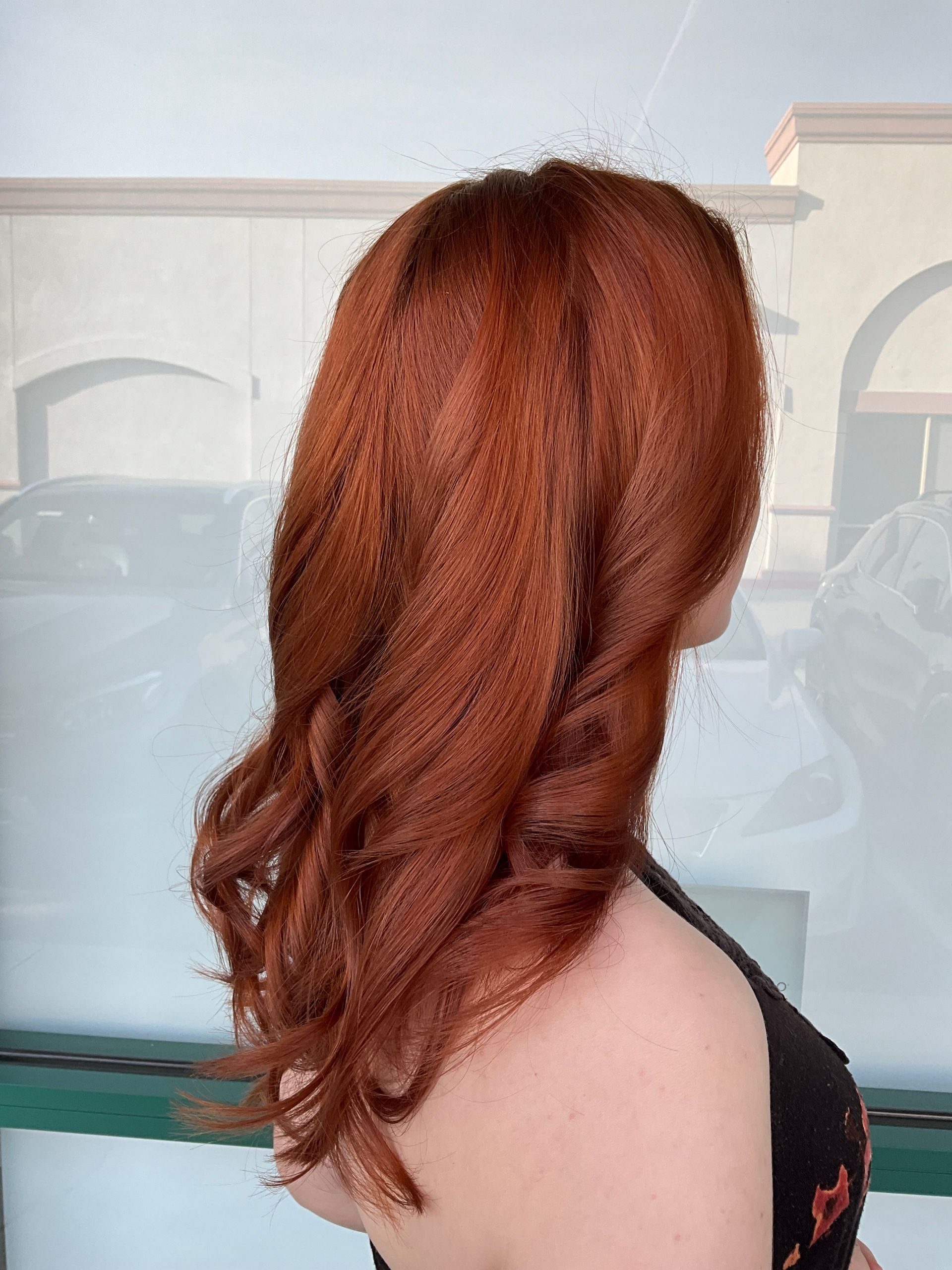 A woman with long red hair is standing in front of a window.