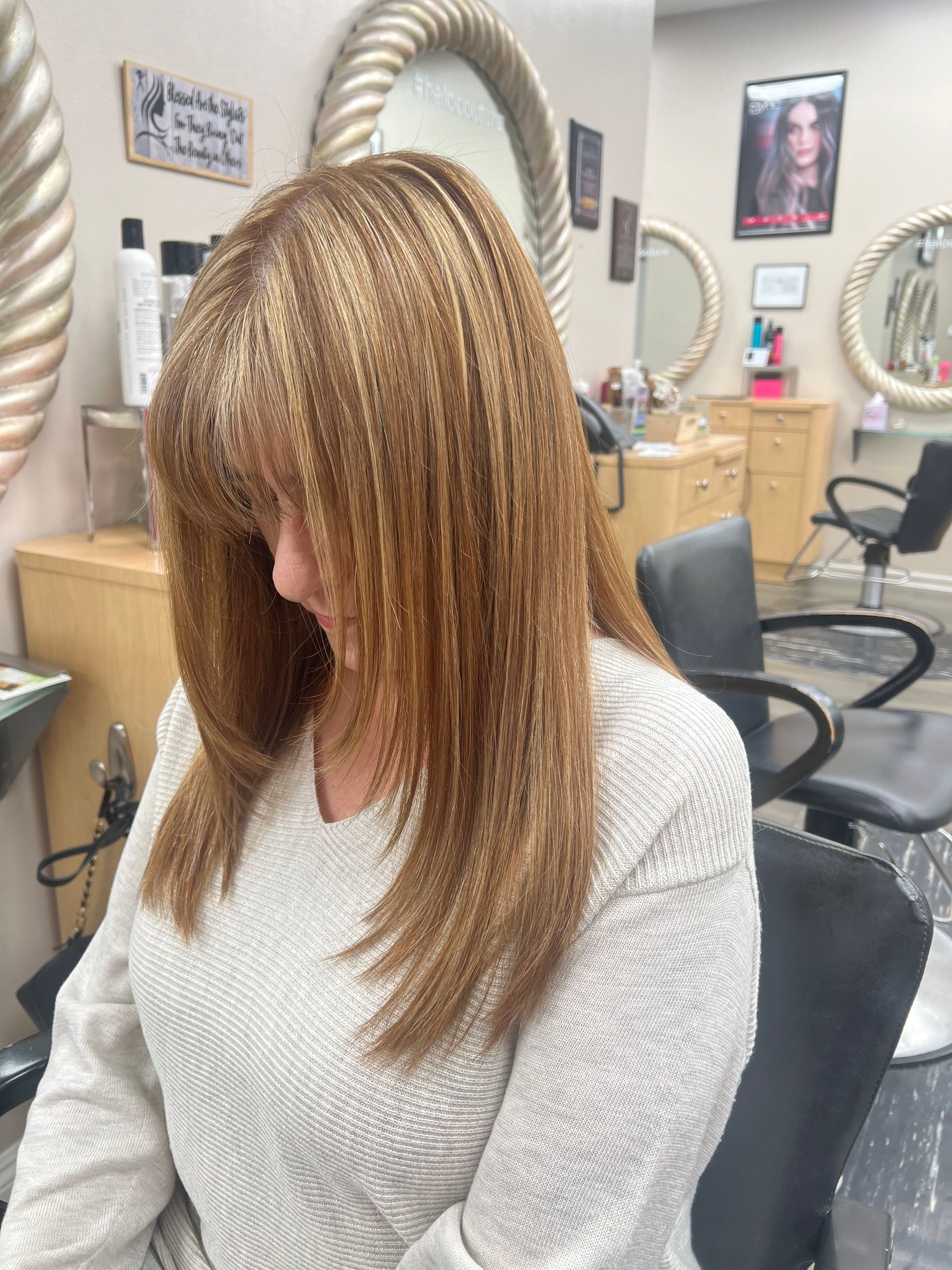 A woman is sitting in a chair in a salon with her head down.