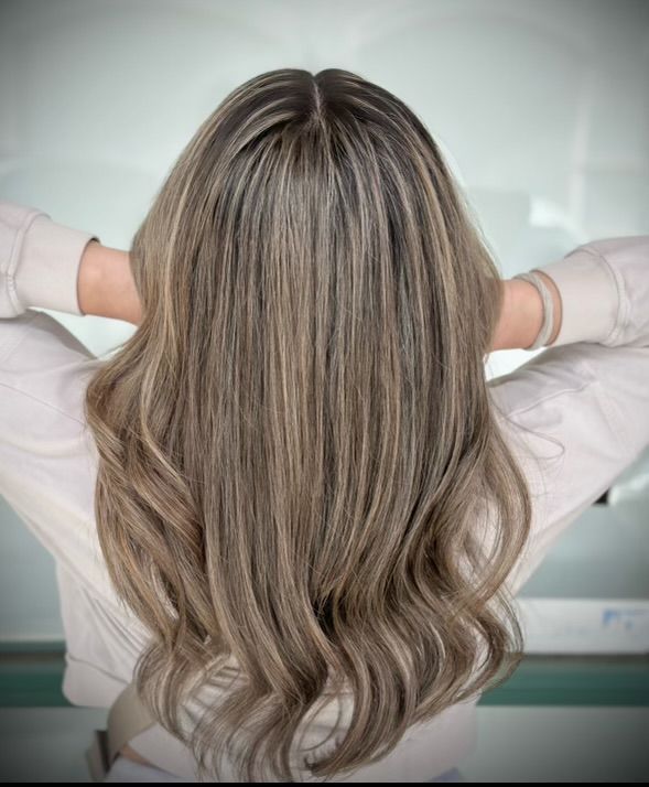 A woman with long wavy hair is sitting with her hands behind her head.