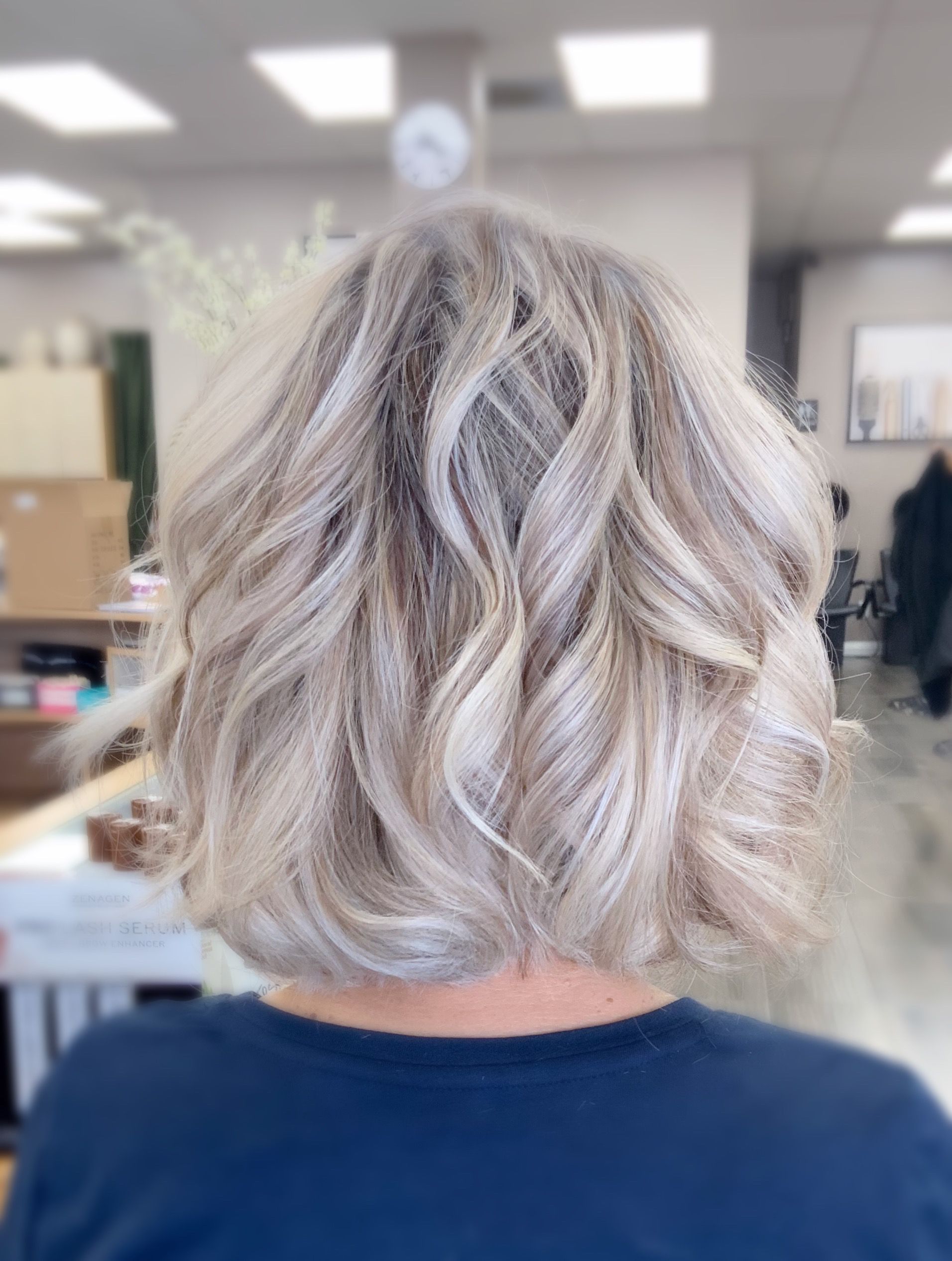 The back of a woman 's head with blonde hair and a blue shirt.
