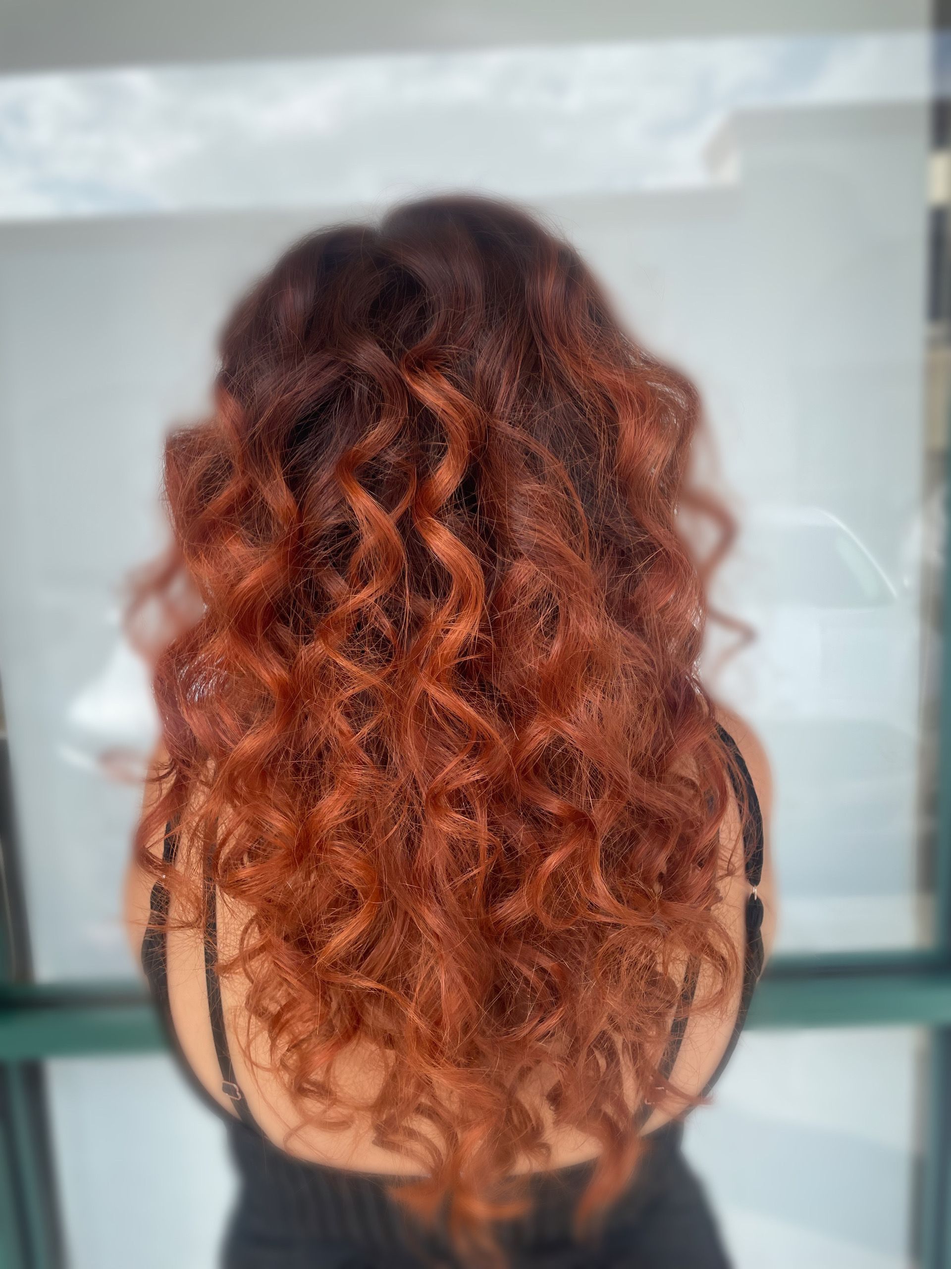 A woman with long red curly hair is standing in front of a window.
