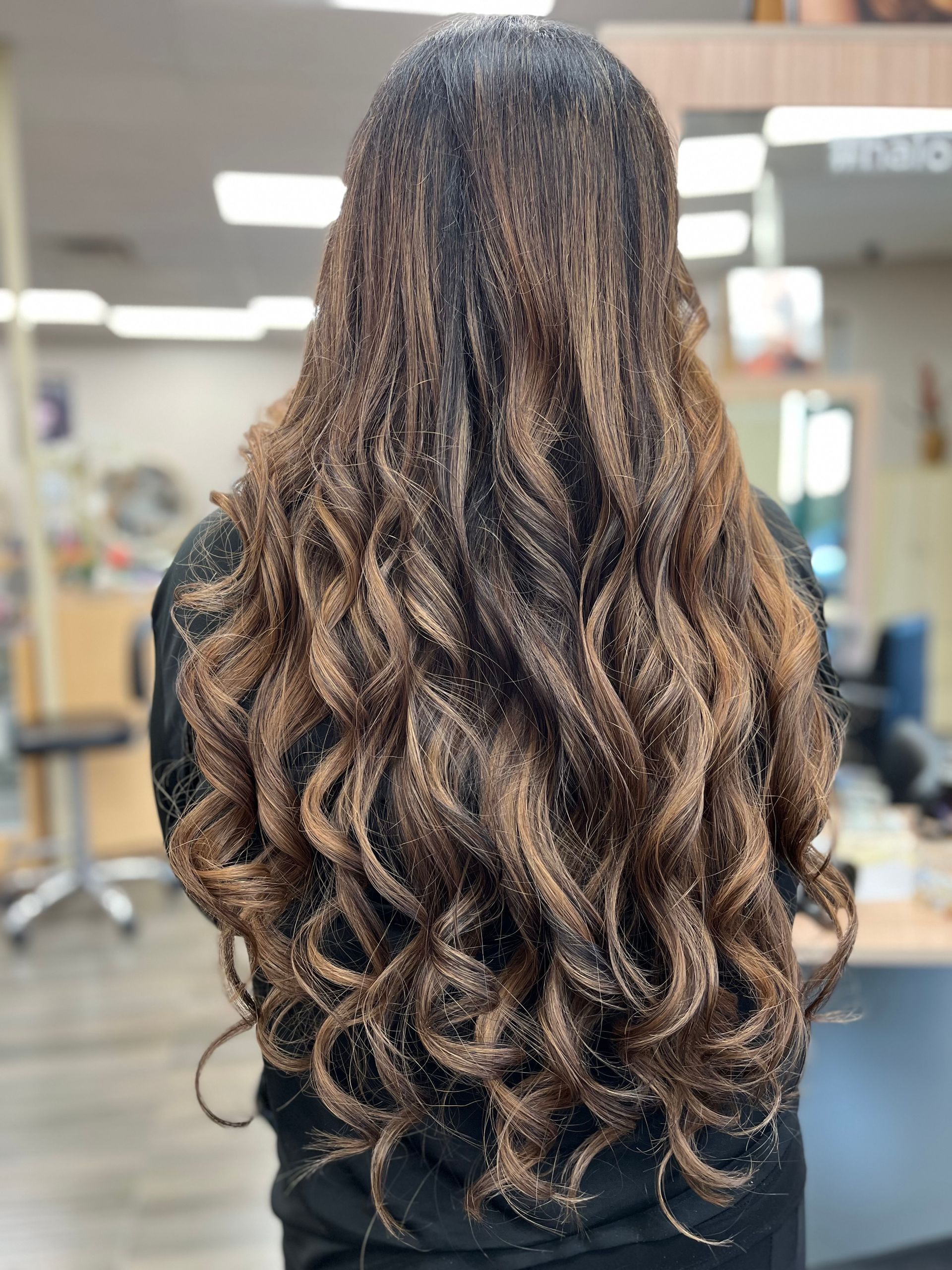 A woman with long curly hair is standing in a salon.