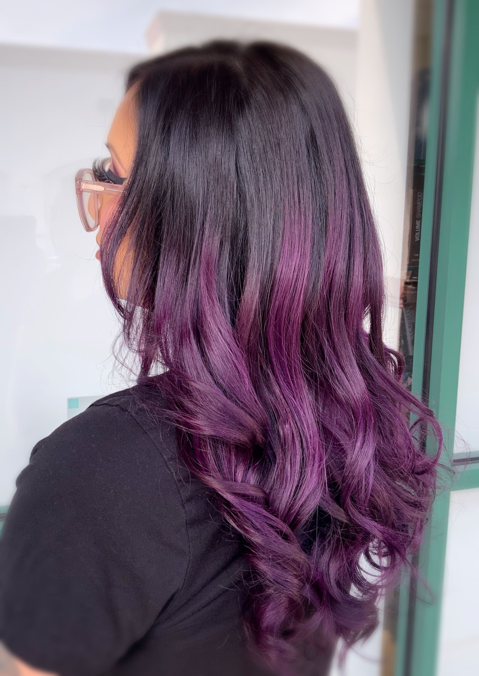 A woman with purple hair is wearing glasses and a black shirt.
