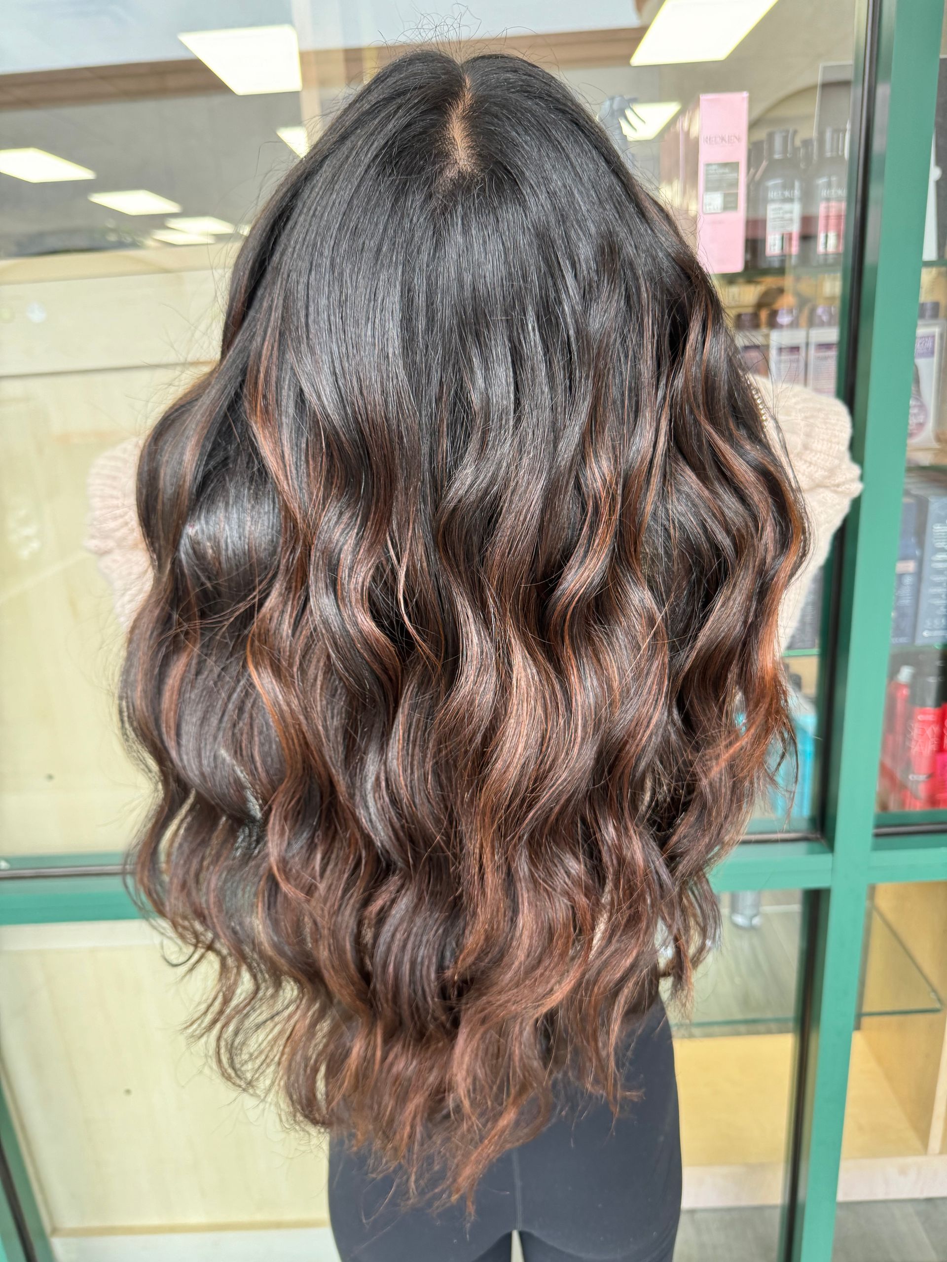 A woman with long wavy brown hair is standing in front of a window.