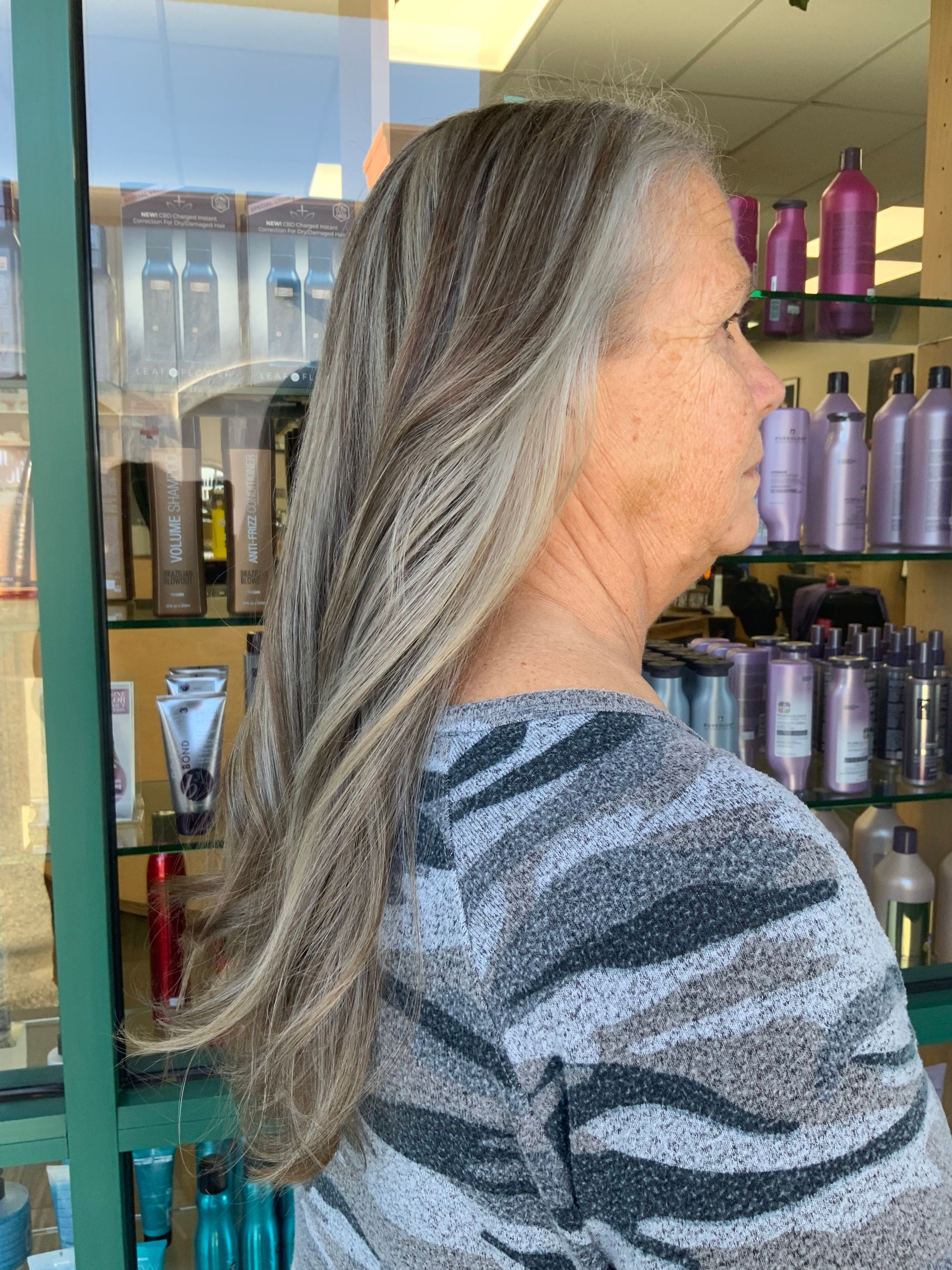 A woman with long gray hair is standing in front of a display of hair products.