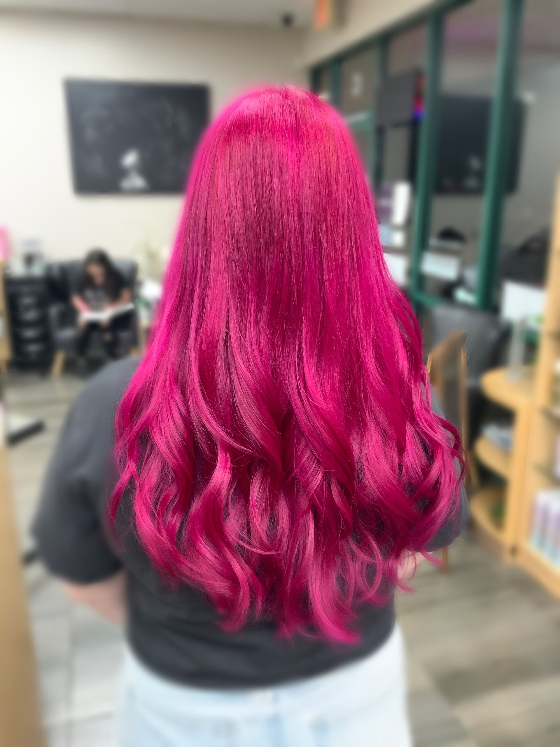 A woman with bright pink hair is standing in a salon.