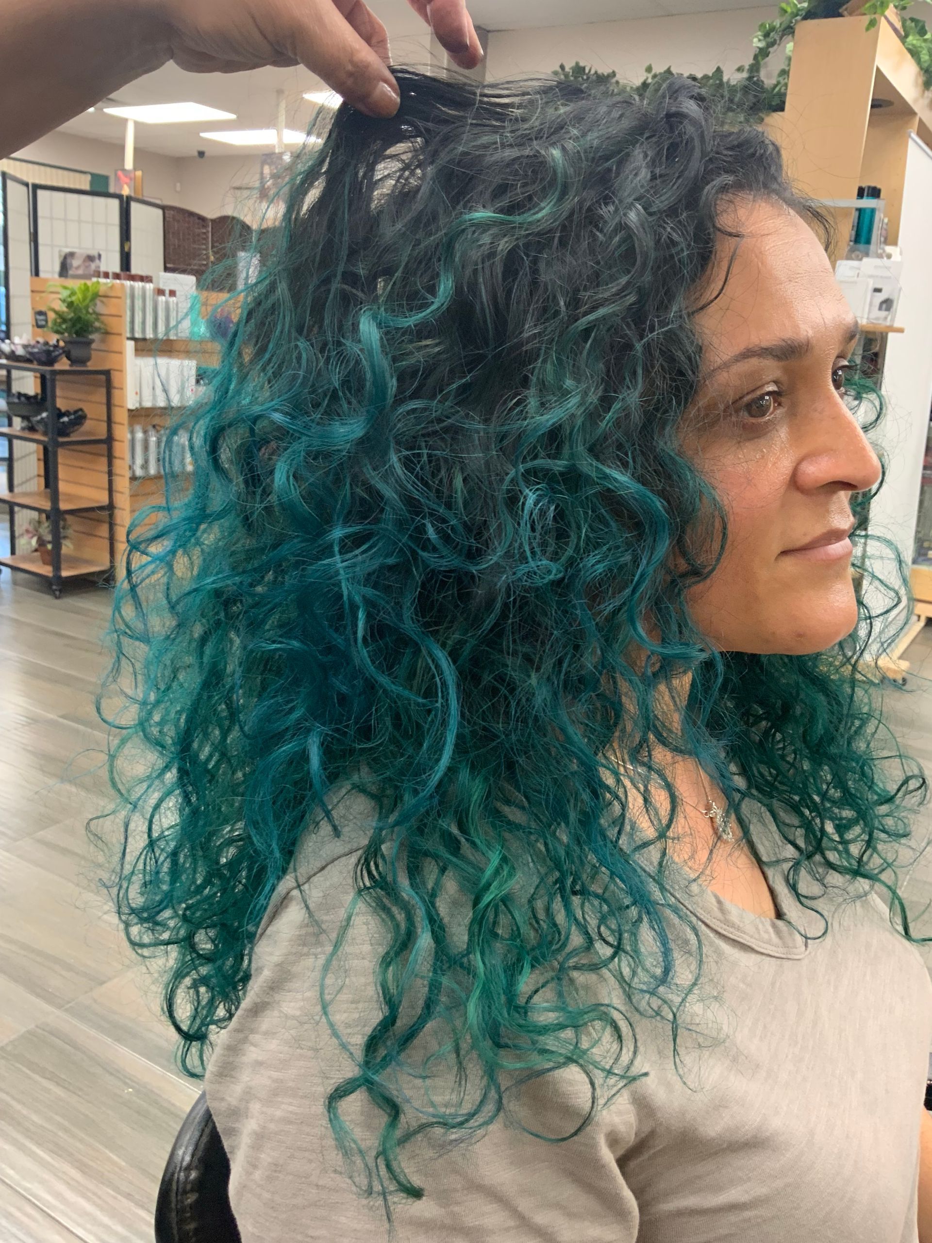 A woman with blue curly hair is getting her hair dyed in a salon.