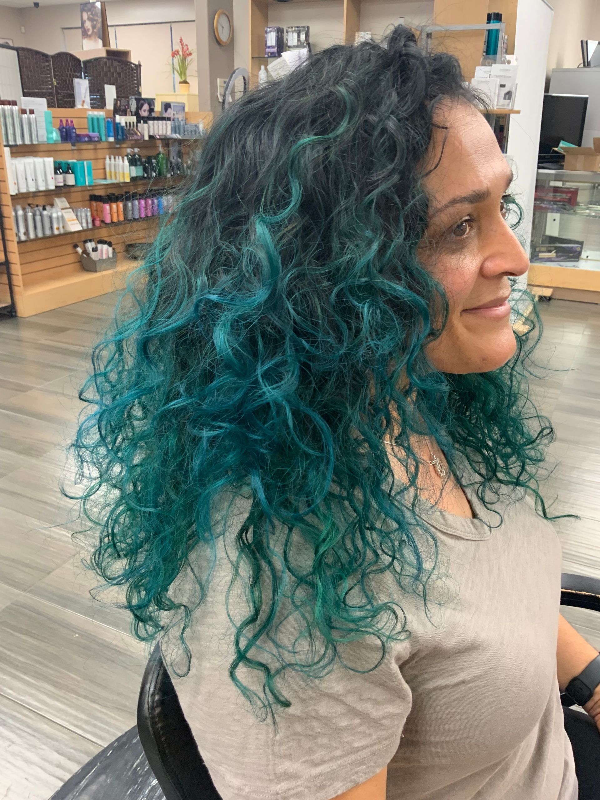 A woman with blue curly hair is sitting in a chair in a salon.