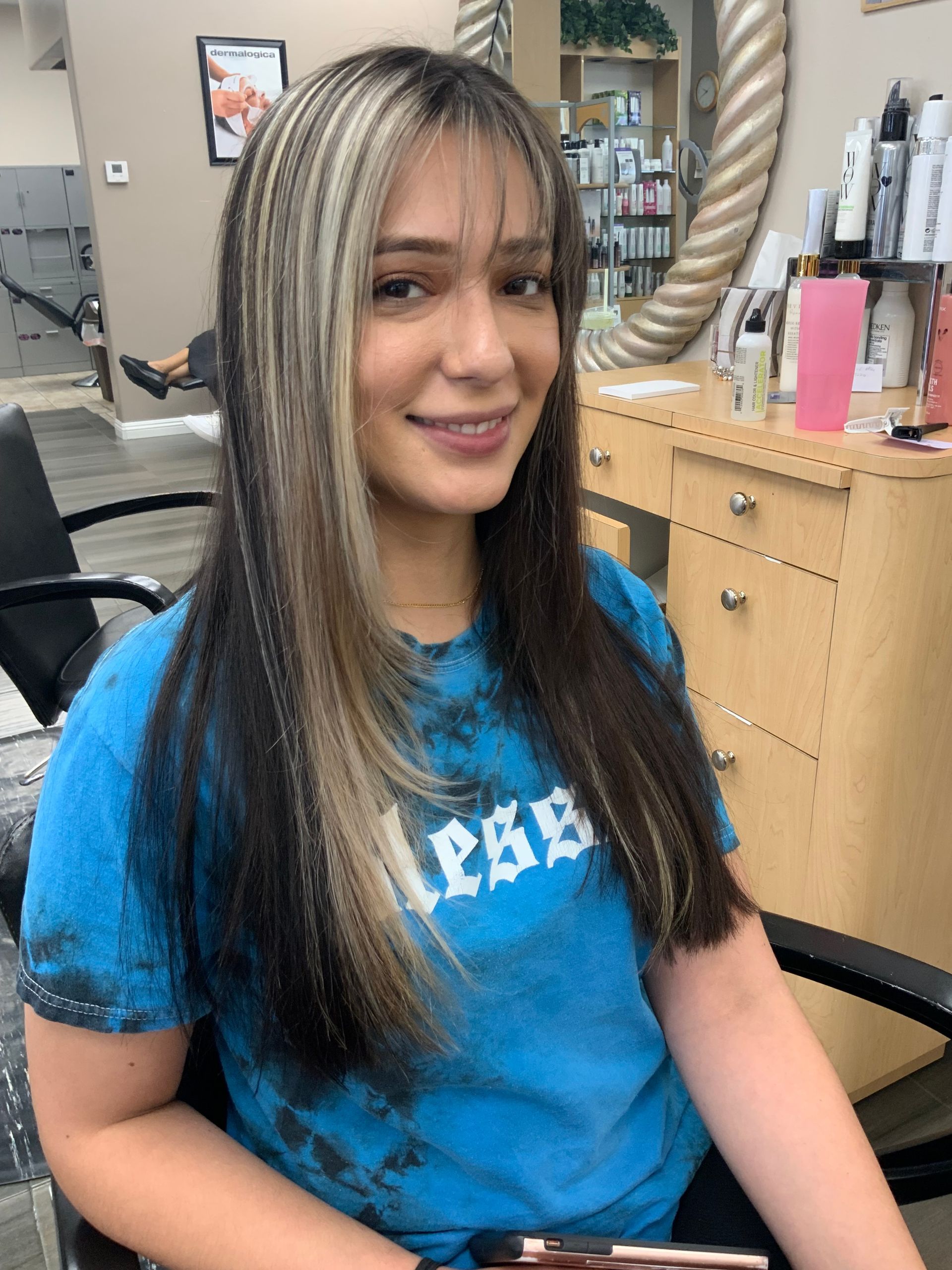 A woman in a blue shirt is sitting in a chair in a salon.