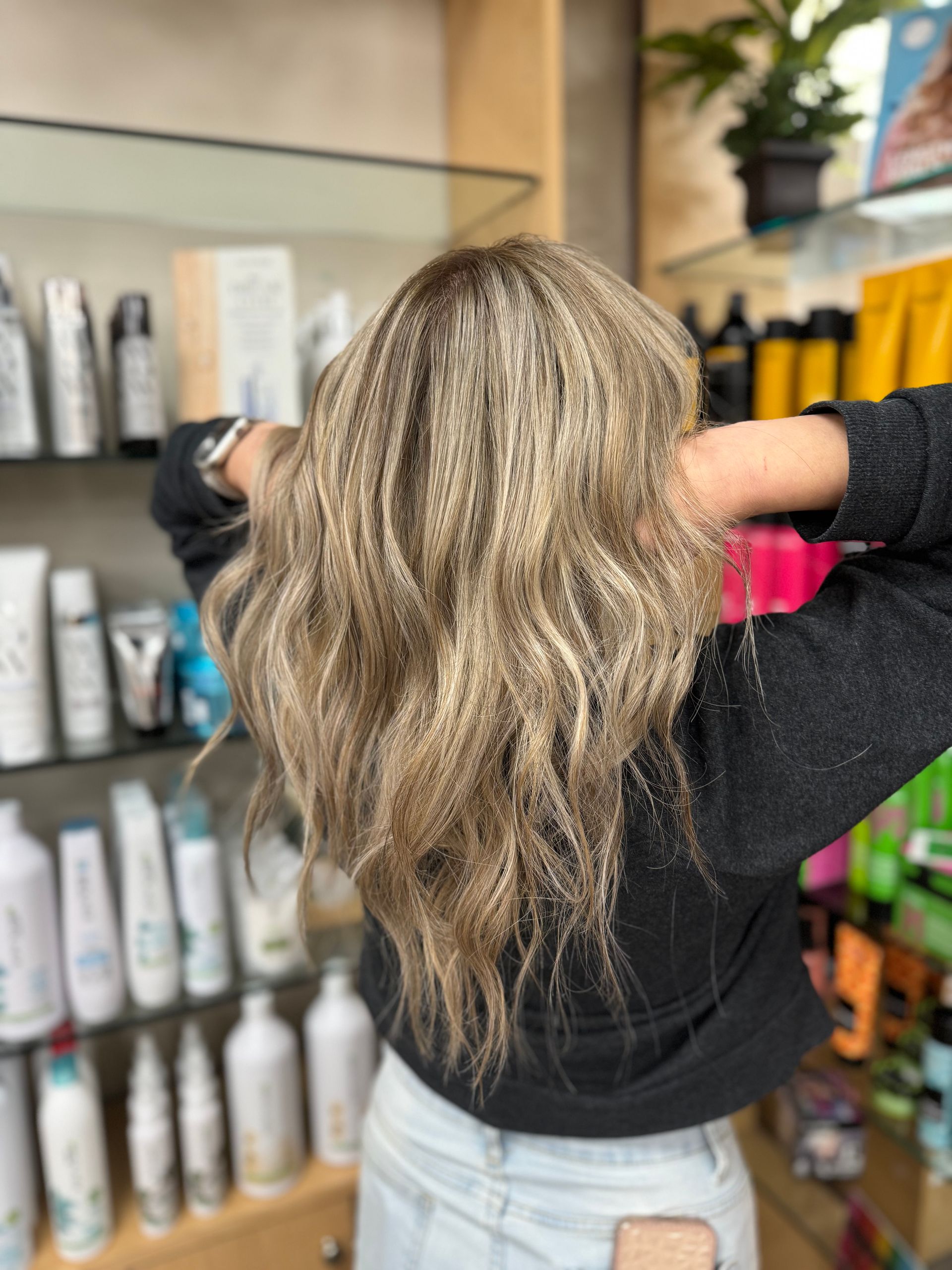 A woman is standing in front of a shelf of hair products in a salon.