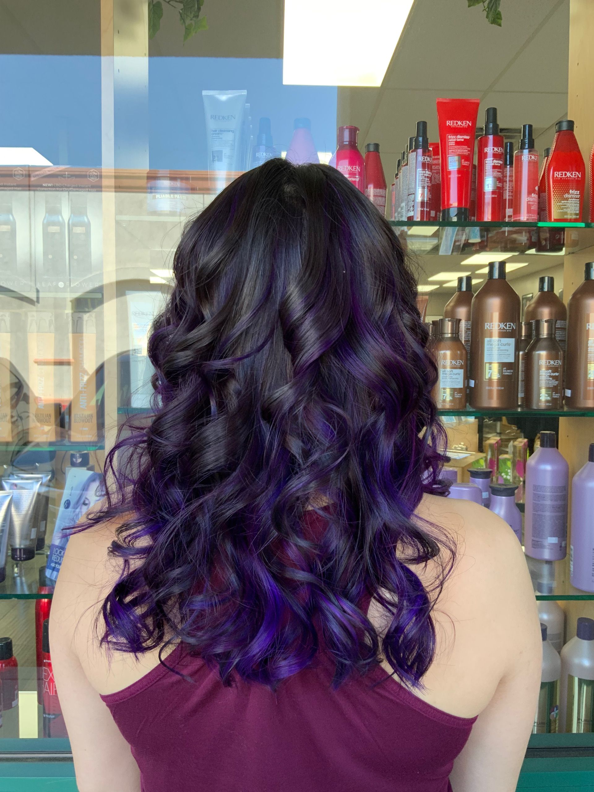 A woman with purple hair is standing in front of a window