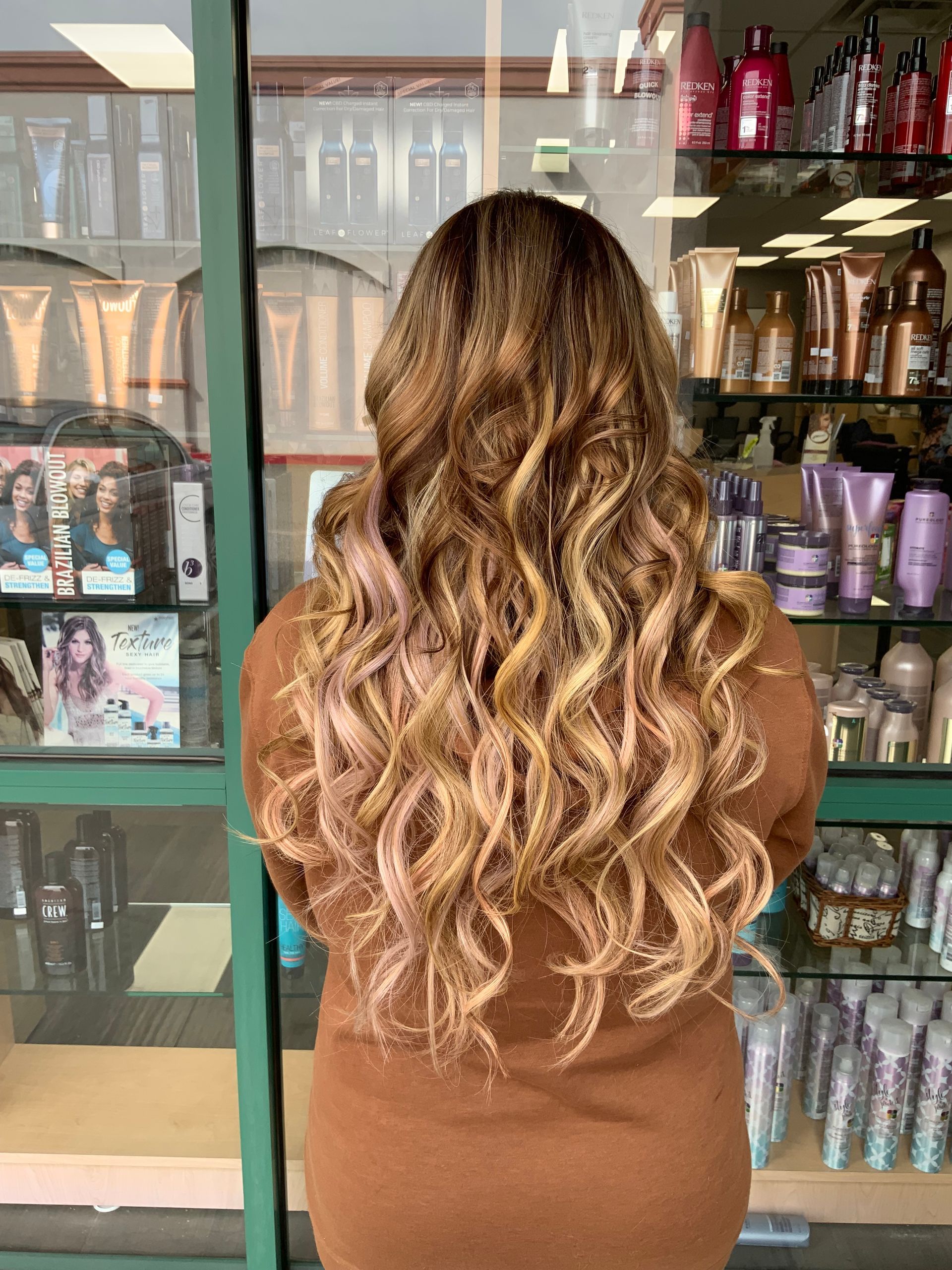 A woman with long wavy hair is standing in front of a store window.