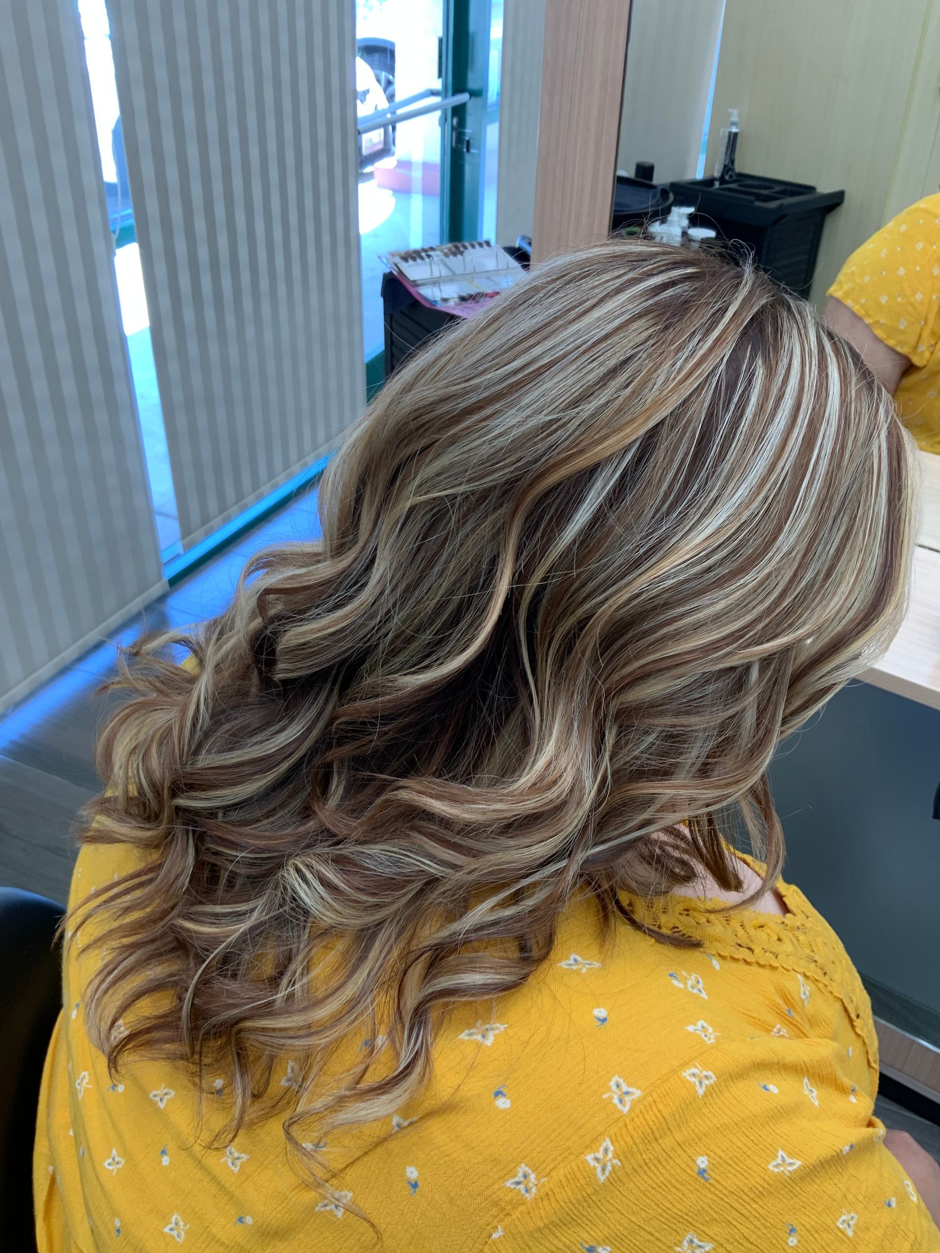 A woman in a yellow shirt is sitting in a chair with her hair in a salon.
