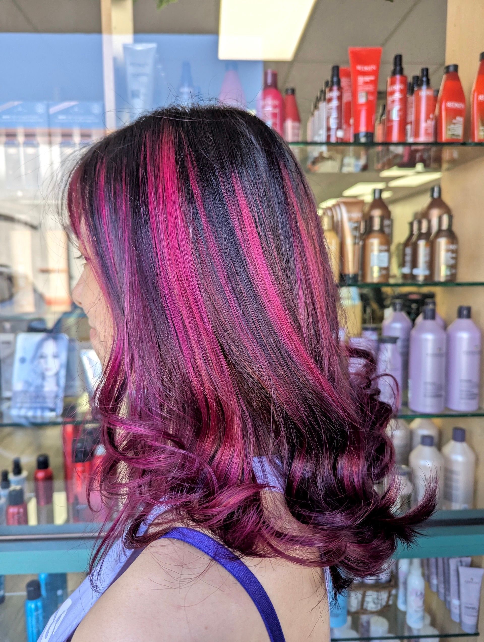 A woman with purple hair is standing in front of a display of hair products