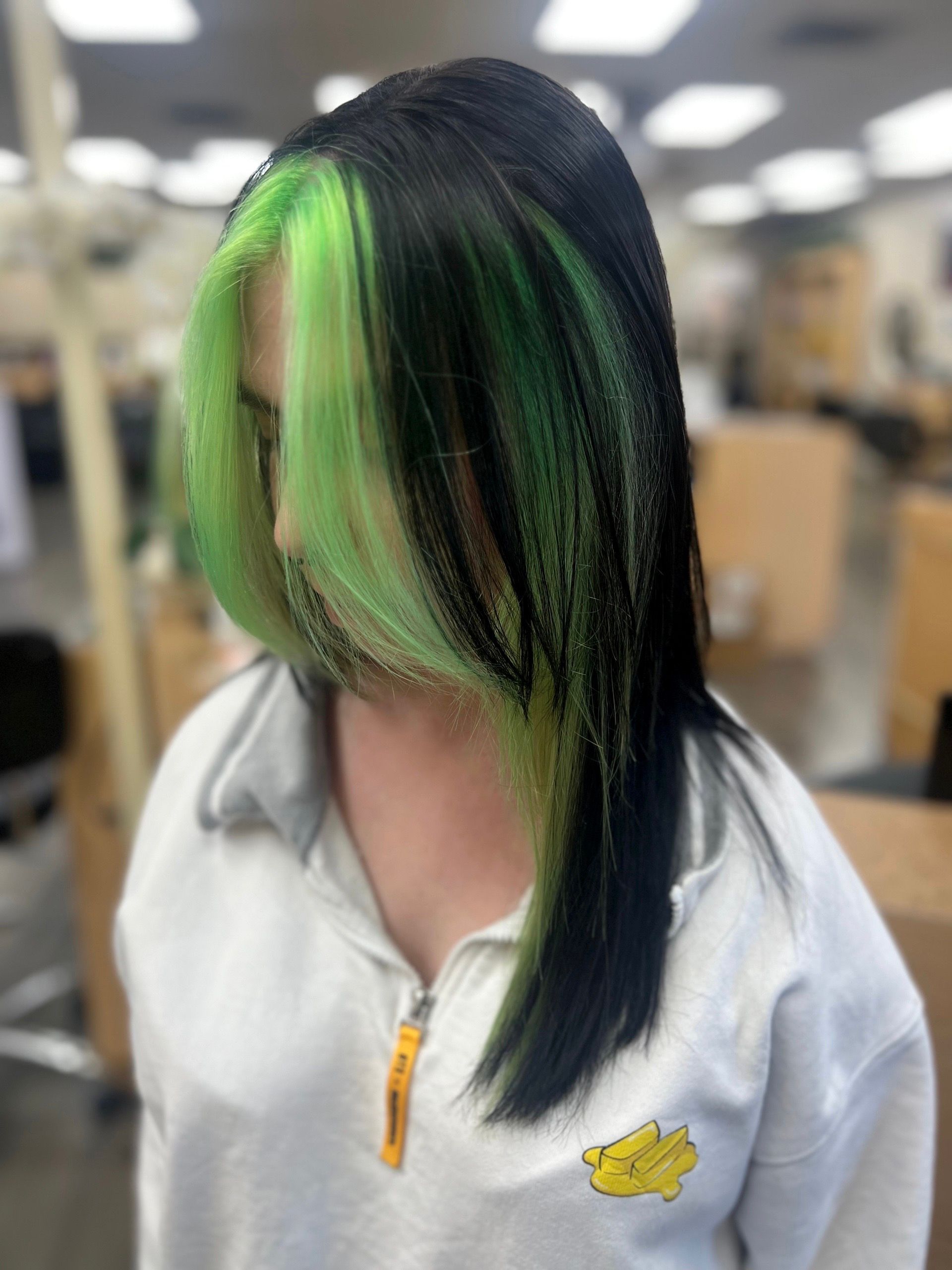 A woman with black hair and green highlights is wearing a white sweatshirt.