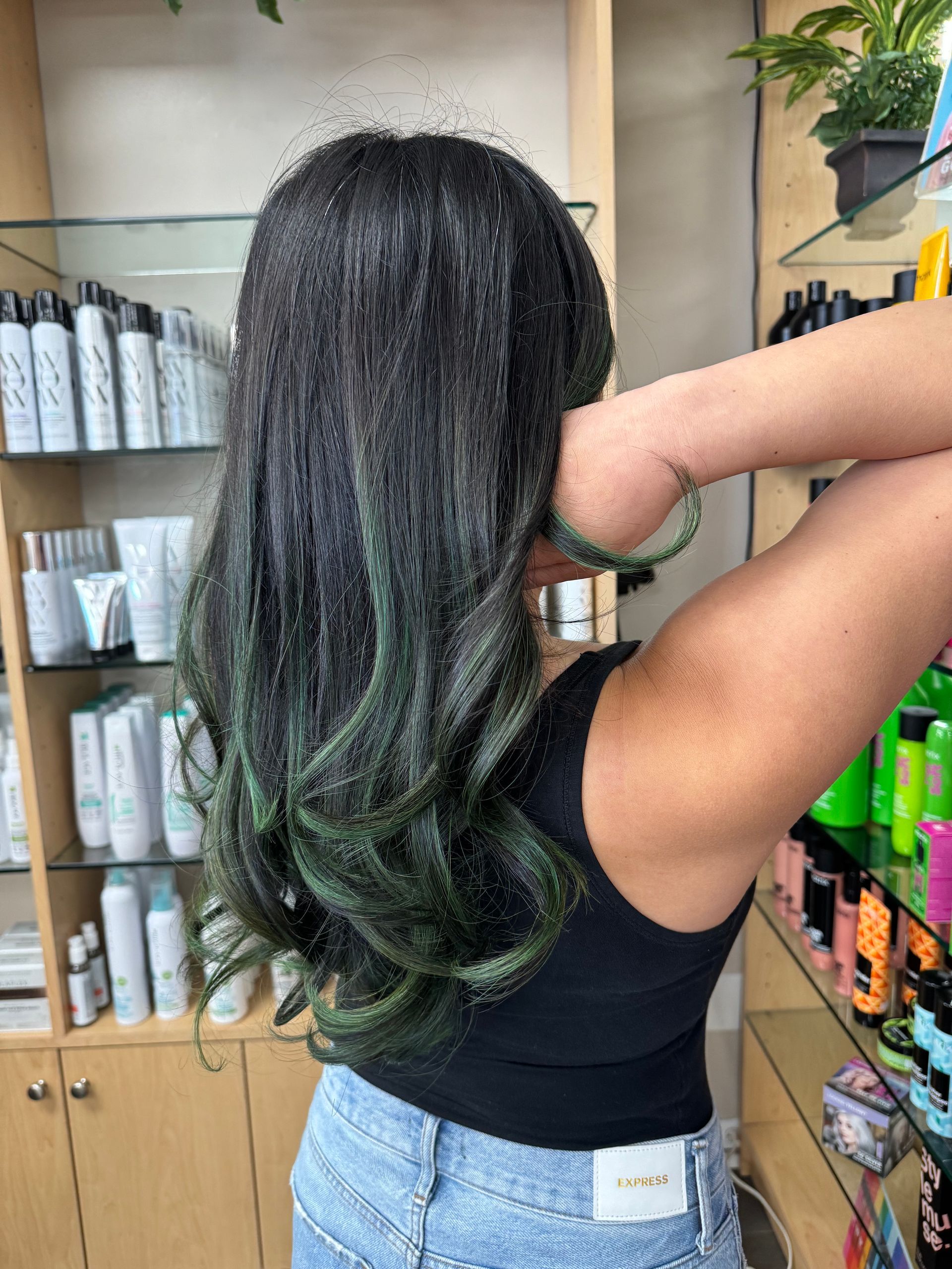 A woman with green hair is standing in a salon.