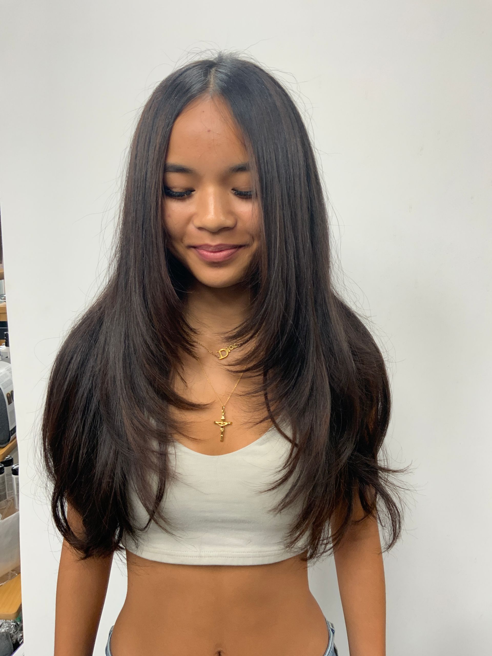 A woman with long hair is wearing a white crop top and a necklace.