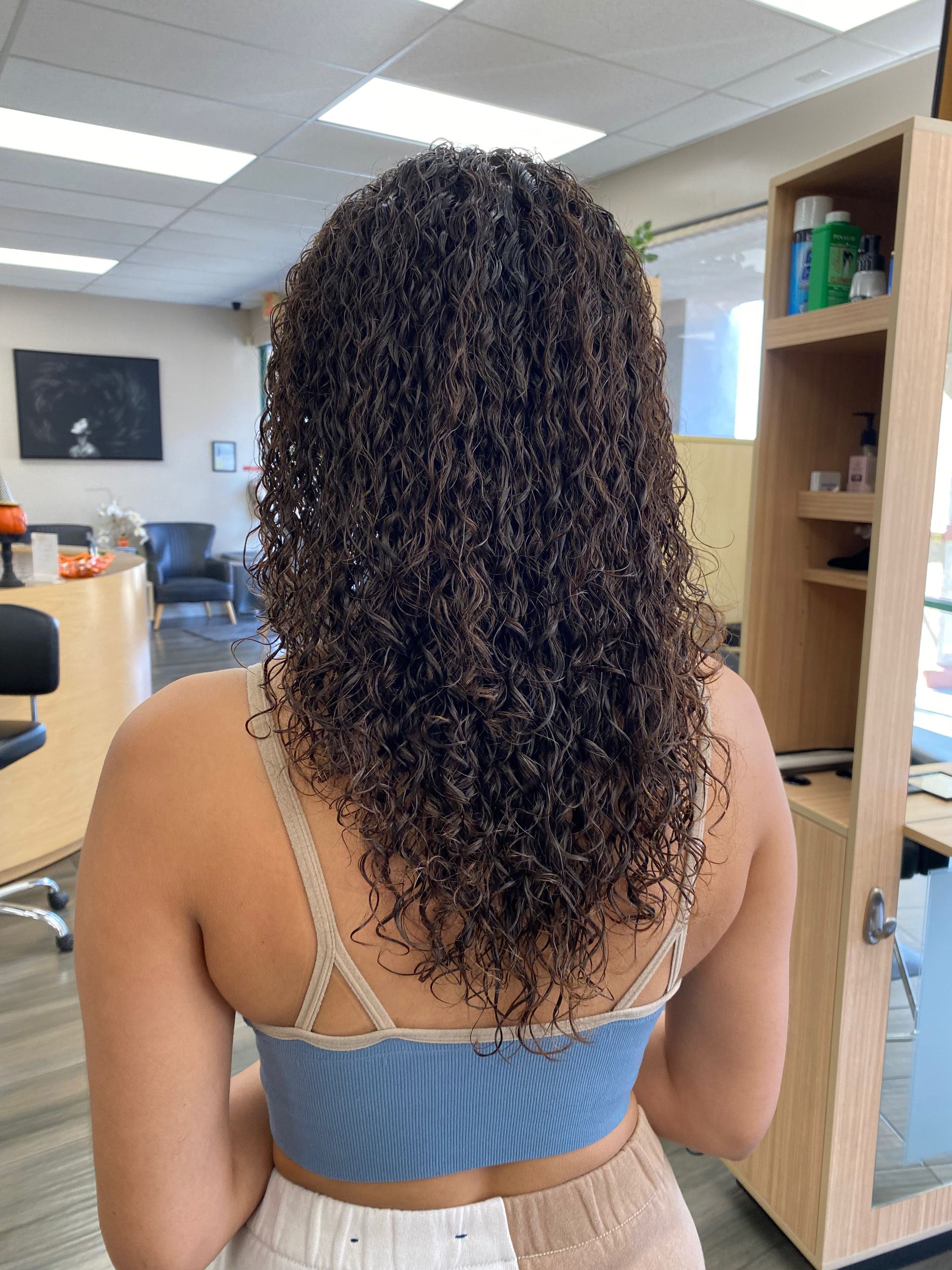 A woman with curly hair is standing in a room wearing a blue tank top.