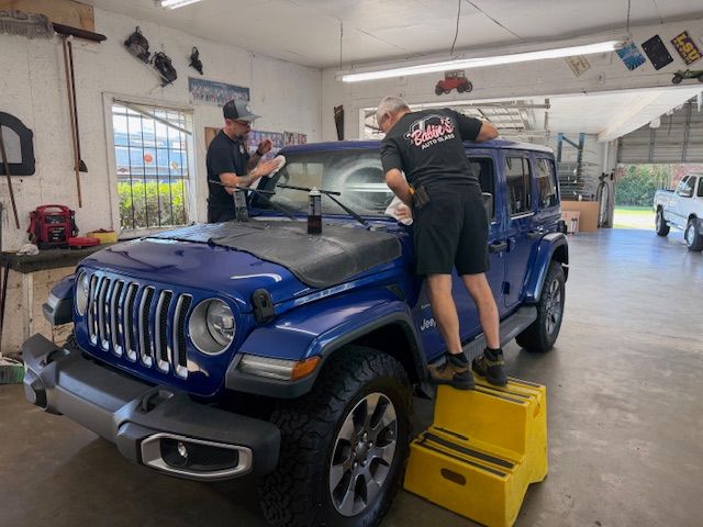 Two people applying tint to a blue Jeep's windows inside a garage.